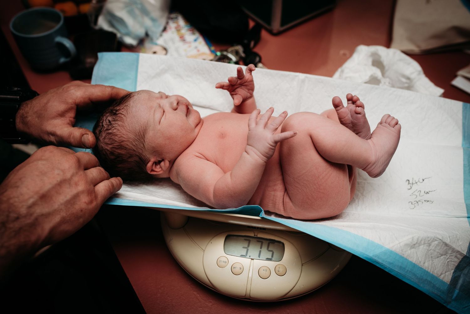 Newborn baby being weighed on a digital scale during medical examination.