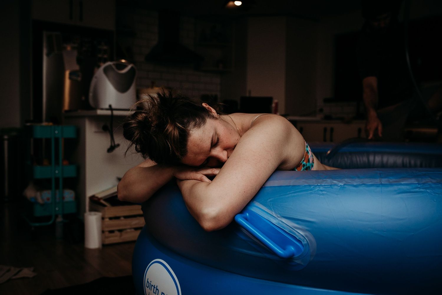Person resting their head on a blue birthing ball in a dimly lit room.