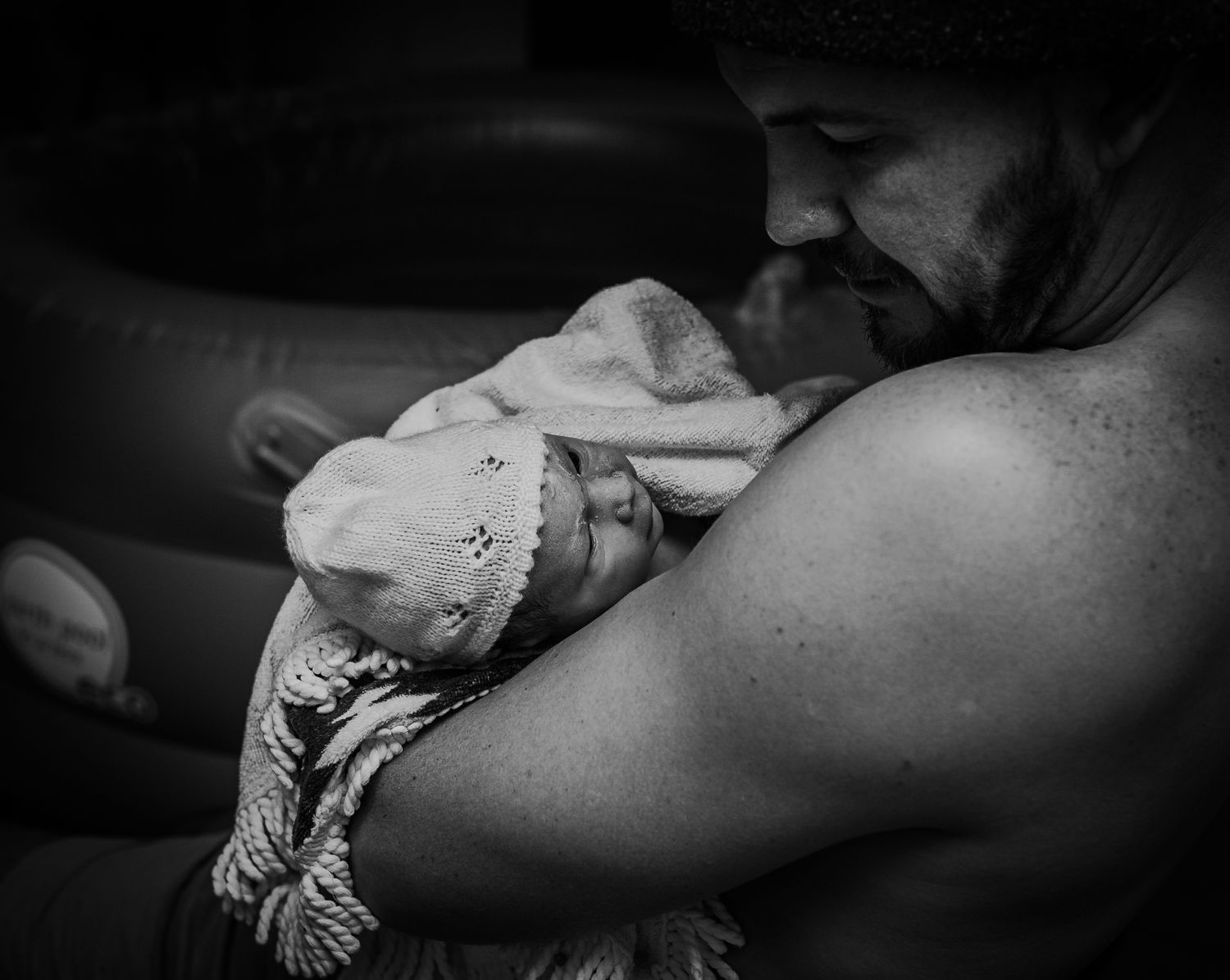 Black and white image of tender moment with newborn wrapped in blanket.