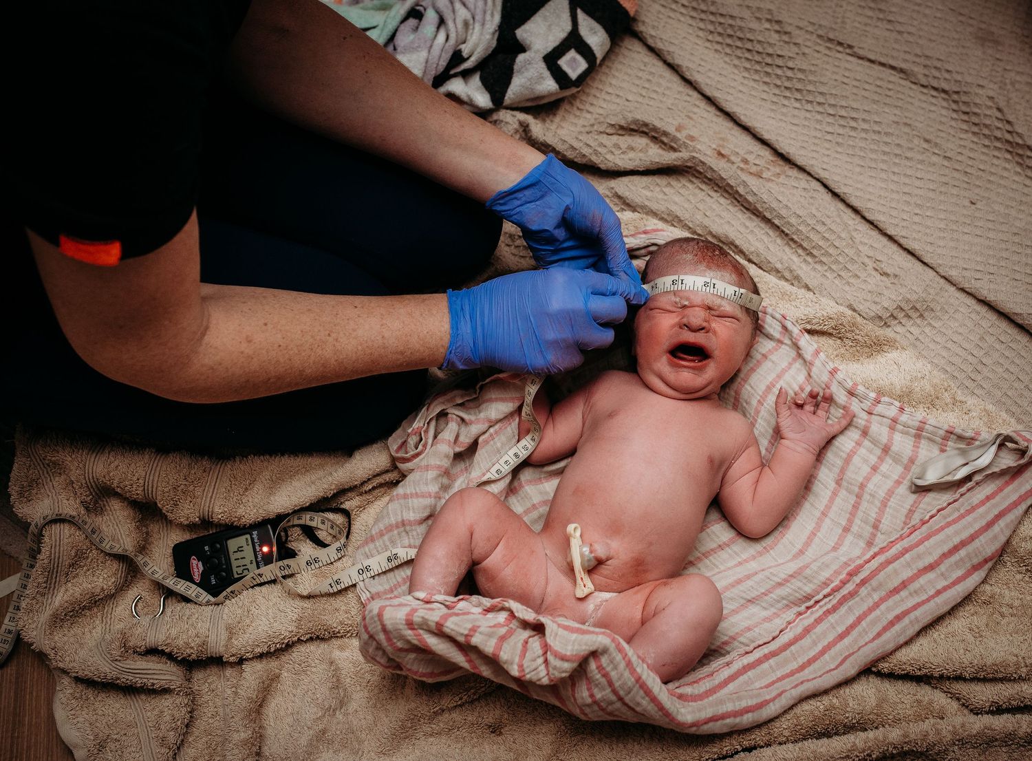 Medical professionals in blue gloves examining a newborn on a beige blanket.