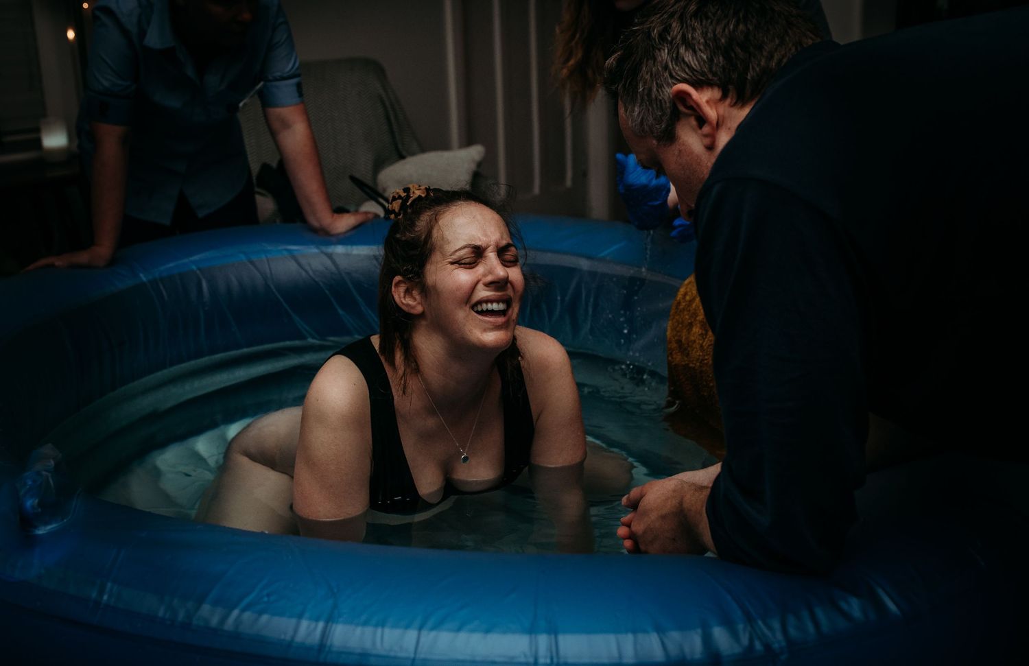 Natural birthing scene in dark setting with supportive care.