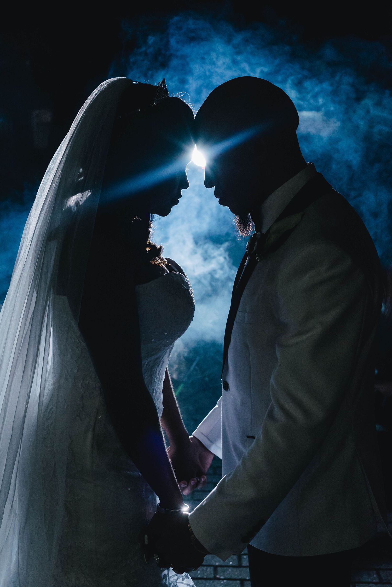 Artistic silhouette of newlyweds with dramatic backlighting and blue smoke creating a romantic atmosphere.