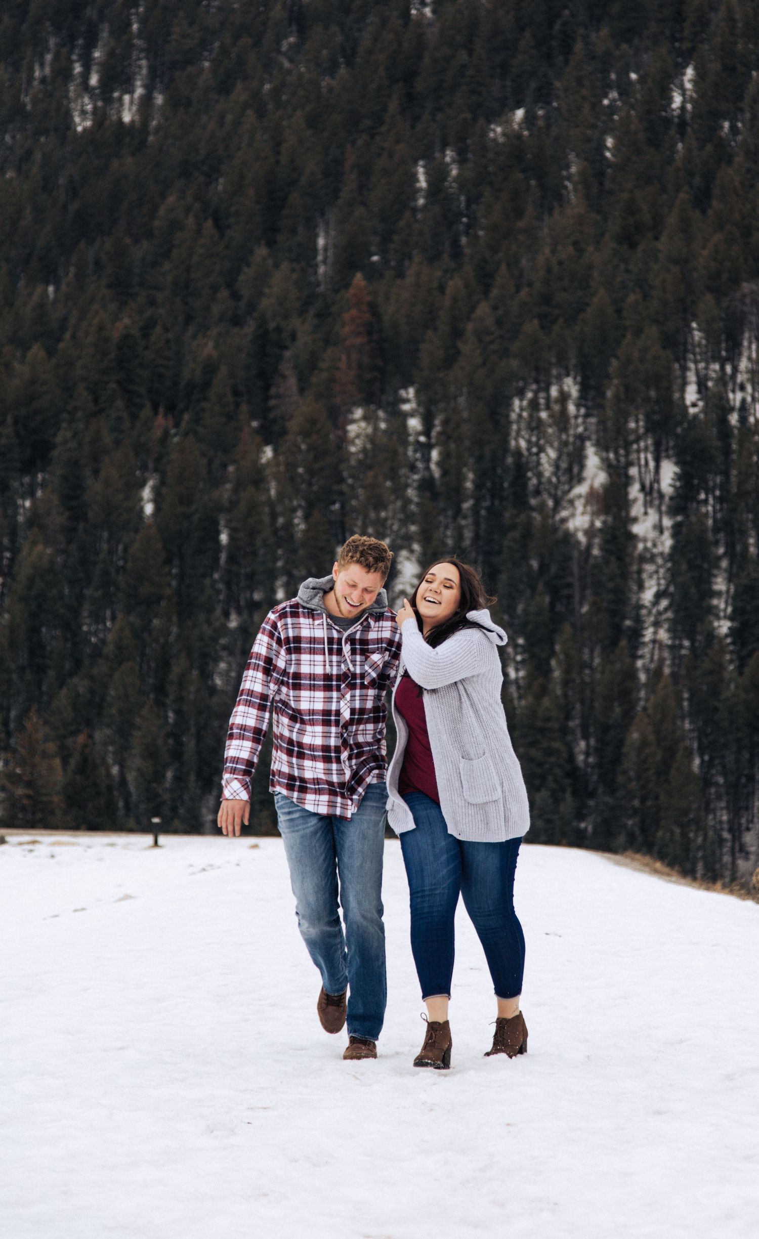 A couple playfully walks through snow with mountain scenery behind them.