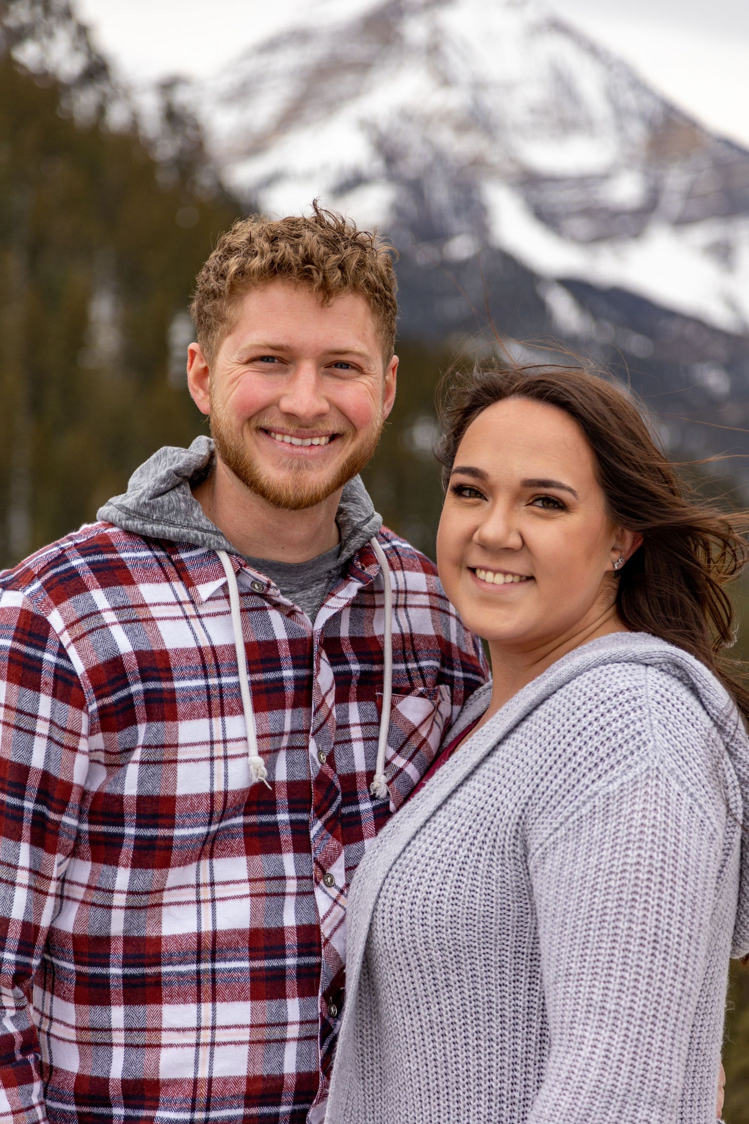 A couple smiles at each other against a dramatic mountain landscape.