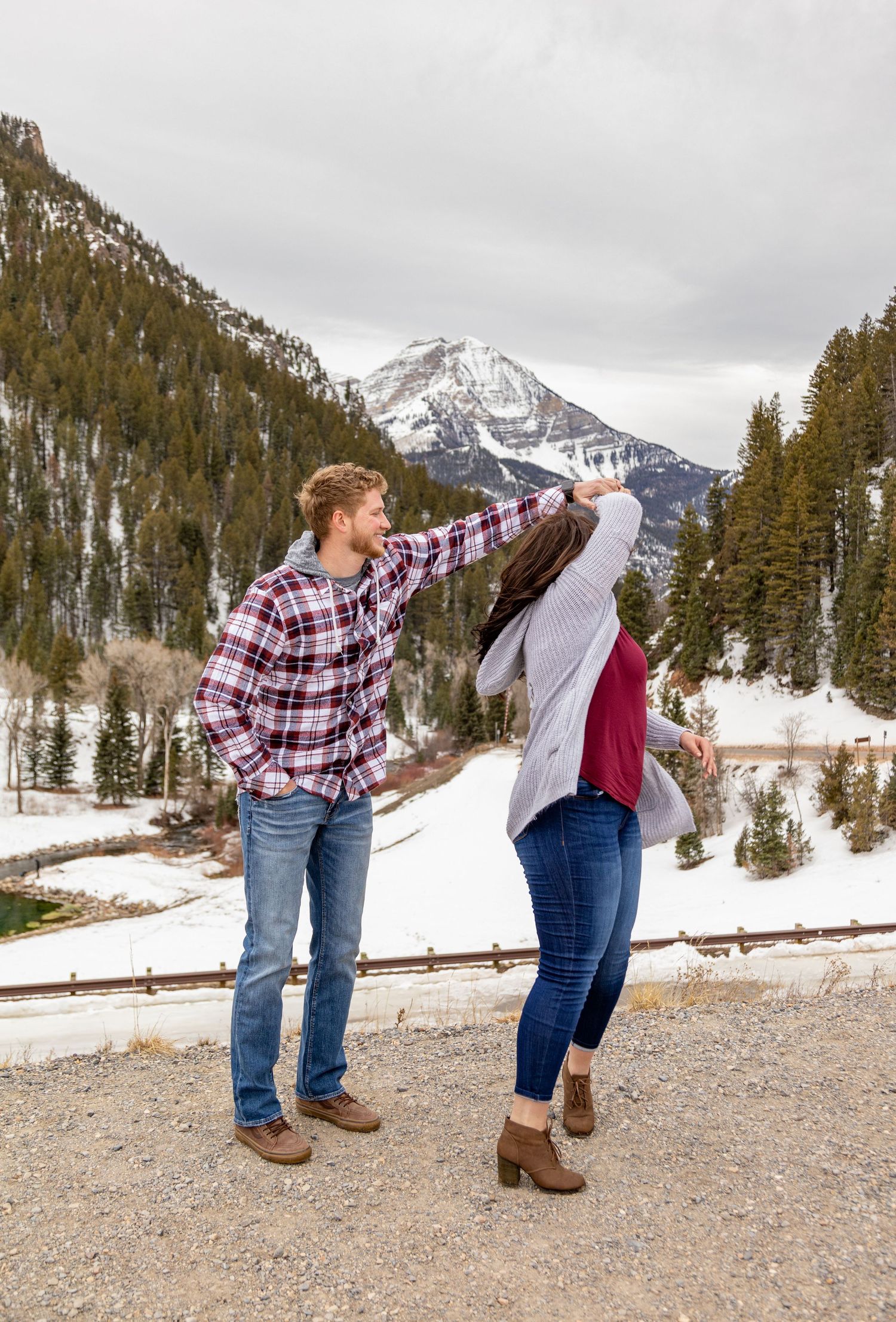 A couple shares a playful moment on a mountain overlook with snowy peaks in the distance.