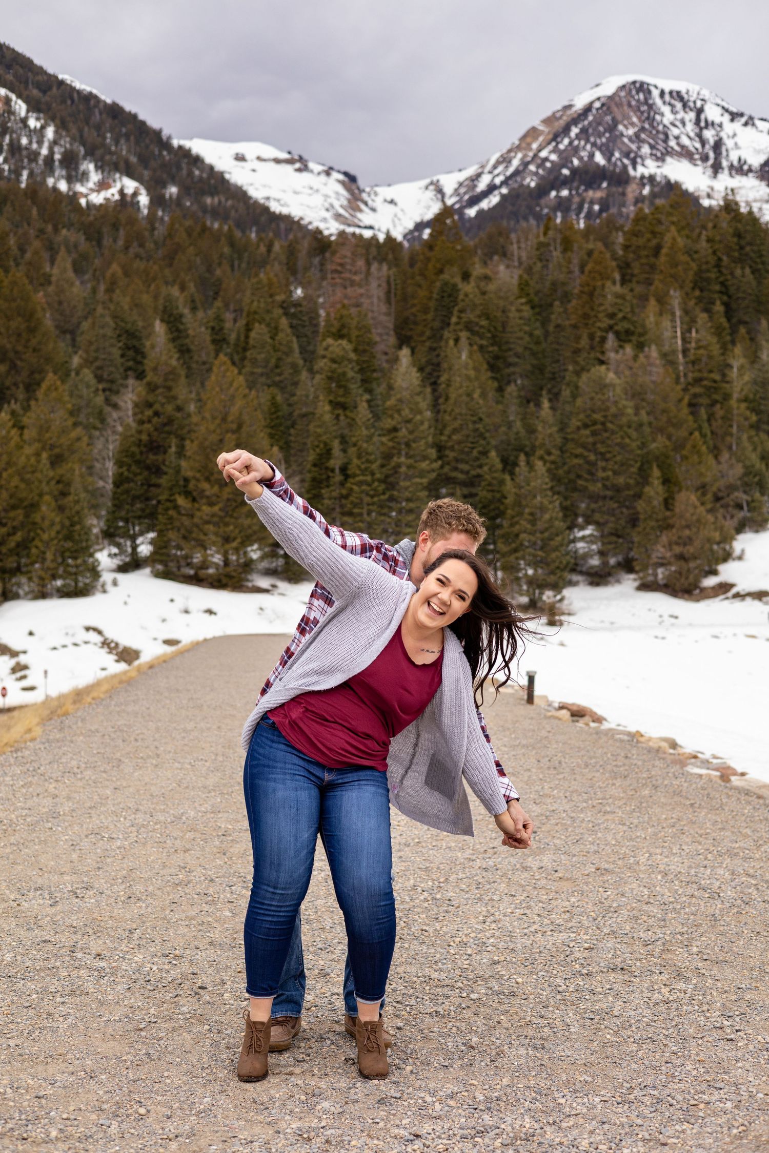 A joyful moment captured on a snowy mountain path surrounded by evergreen trees and snow-capped peaks.
