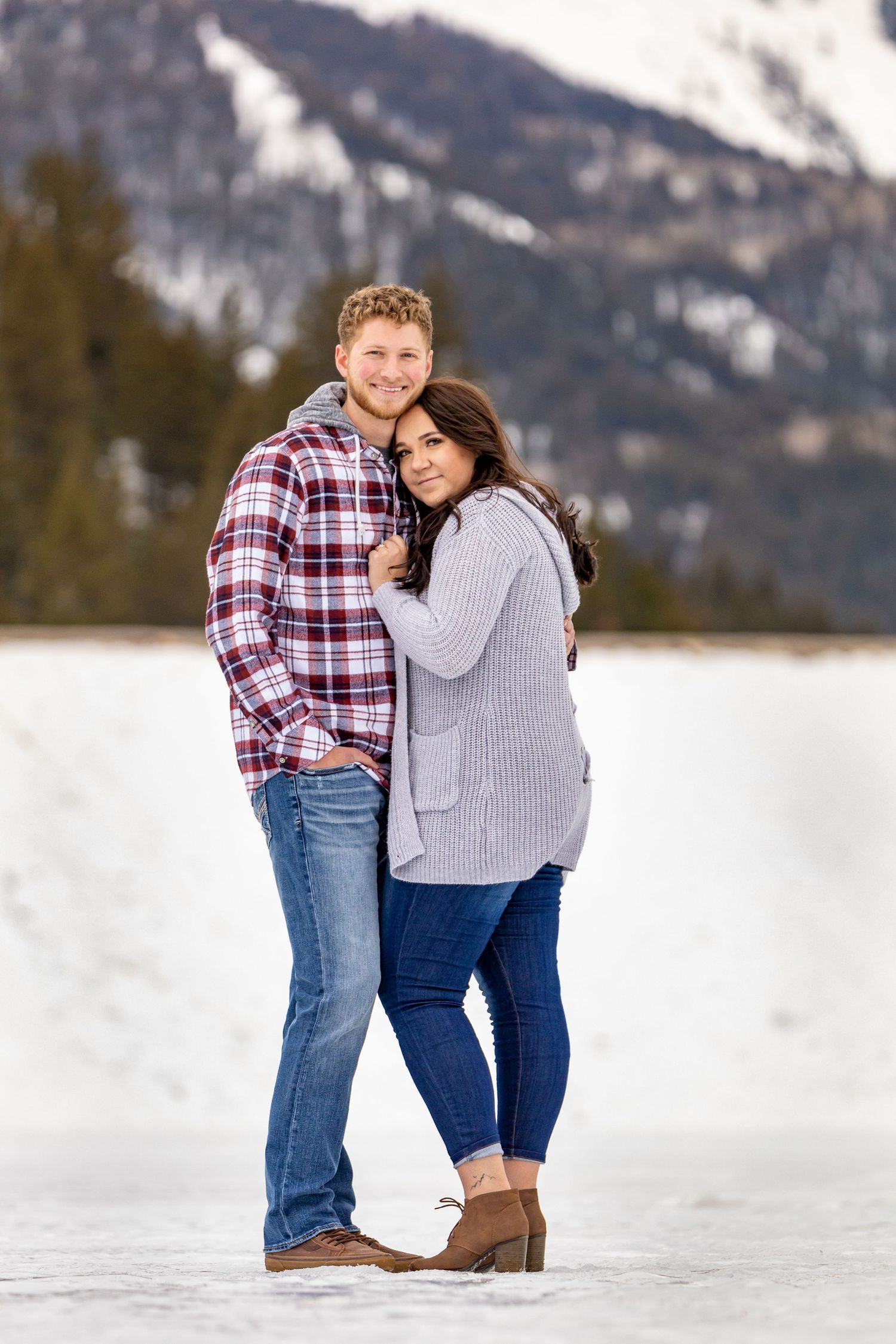 A romantic winter photoshoot with snow-covered mountains and forest in the background.