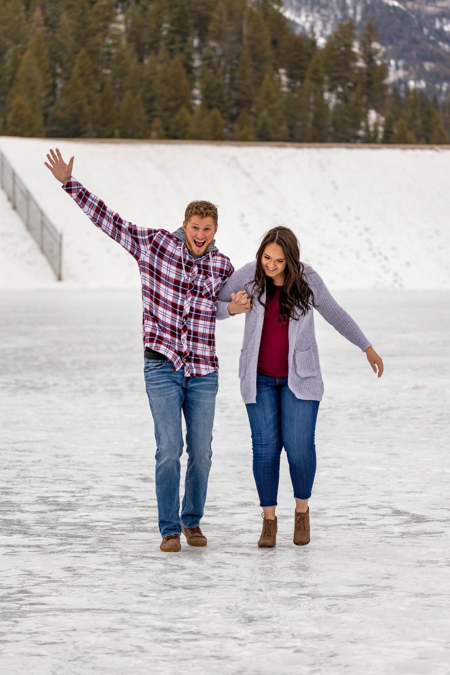 A playful couple walks together on a snowy surface with mountains in the distance.