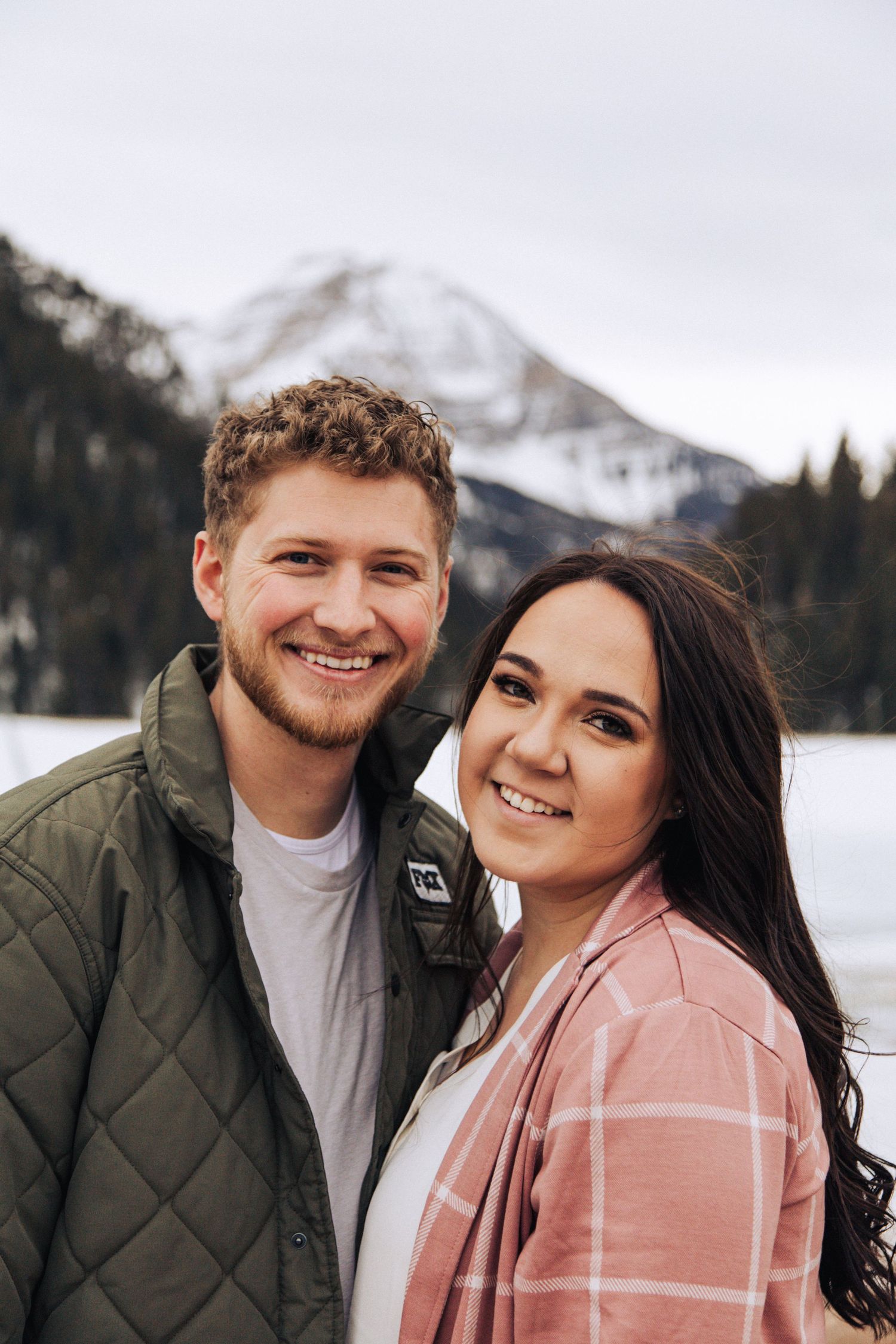 A couple shares a happy moment together with snowy mountains visible in the background.