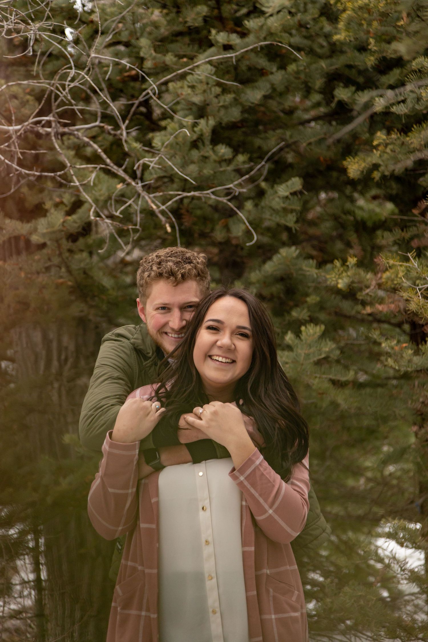 A couple embraces while enjoying an autumn day near a pond with trees in the background.