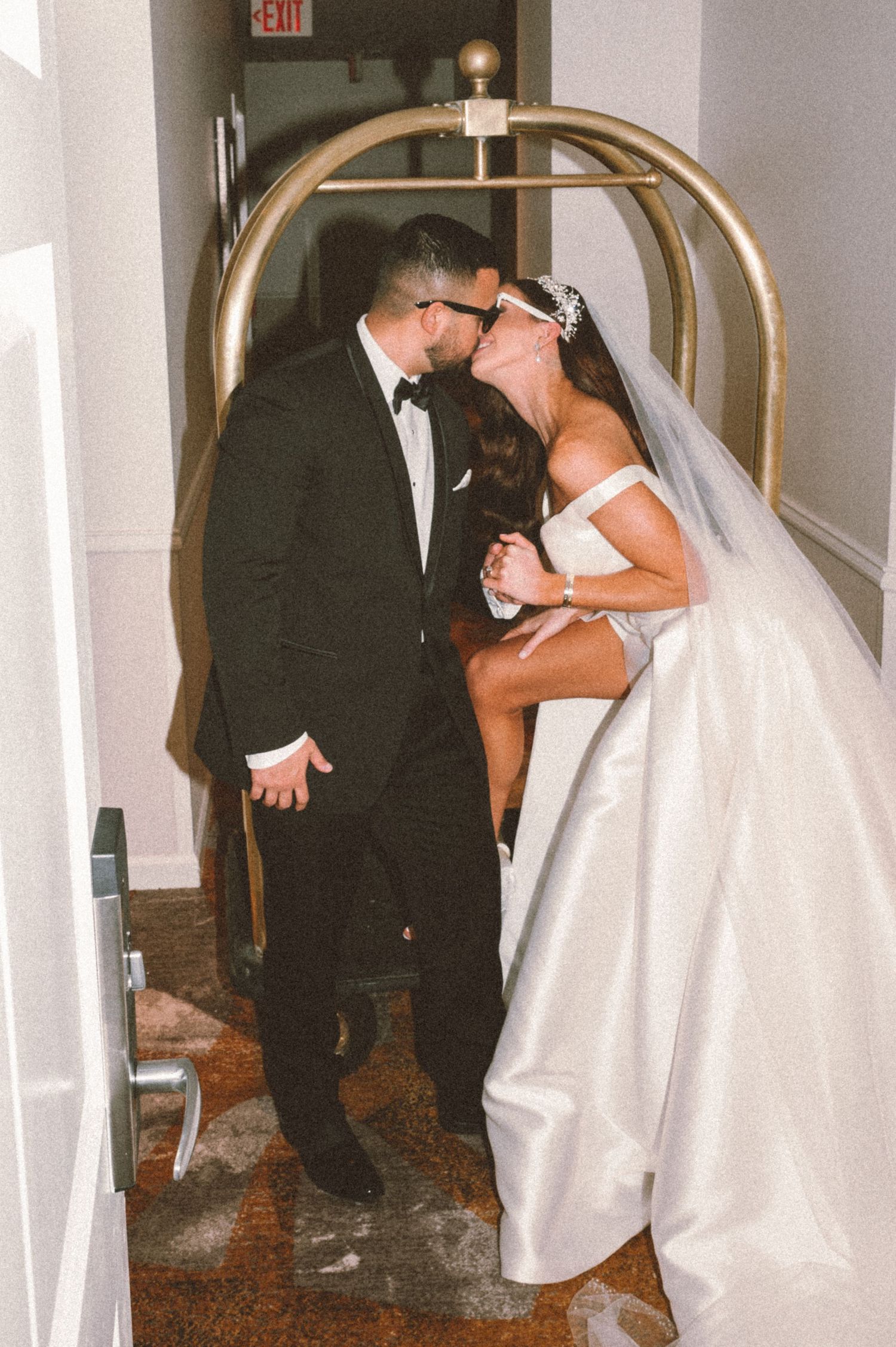 Romantic moment between newlyweds under golden hotel luggage cart arch.