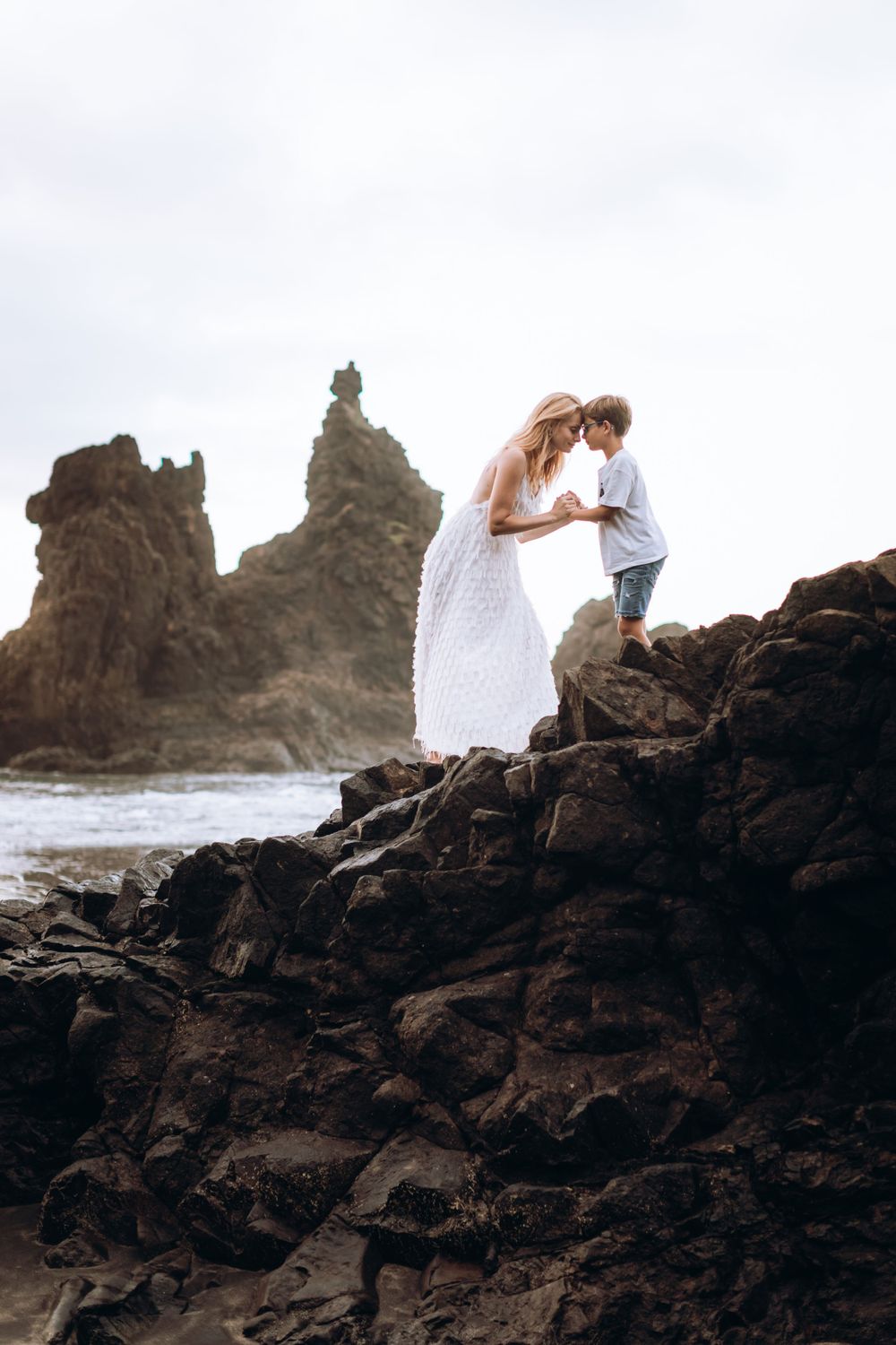 Two figures share a moment on rocky coastal cliffs during sunset.