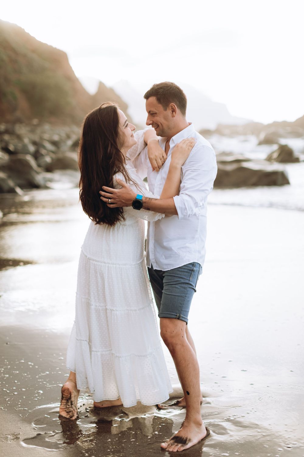 A romantic beach portrait of a couple embracing on the shoreline at sunset.