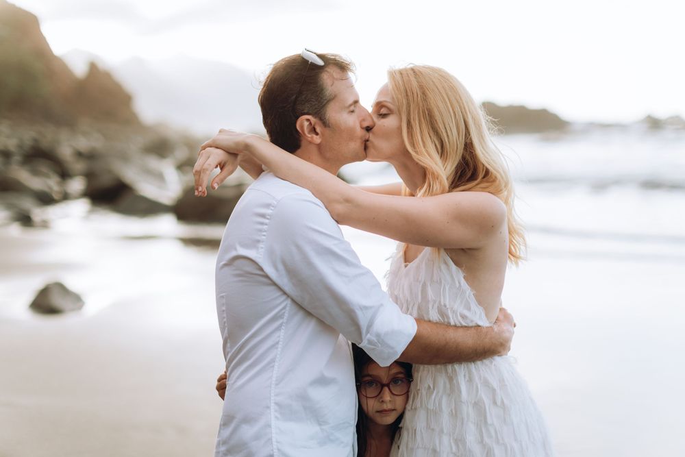 A romantic kiss on the beach with coastal cliffs and ocean waves in the background.