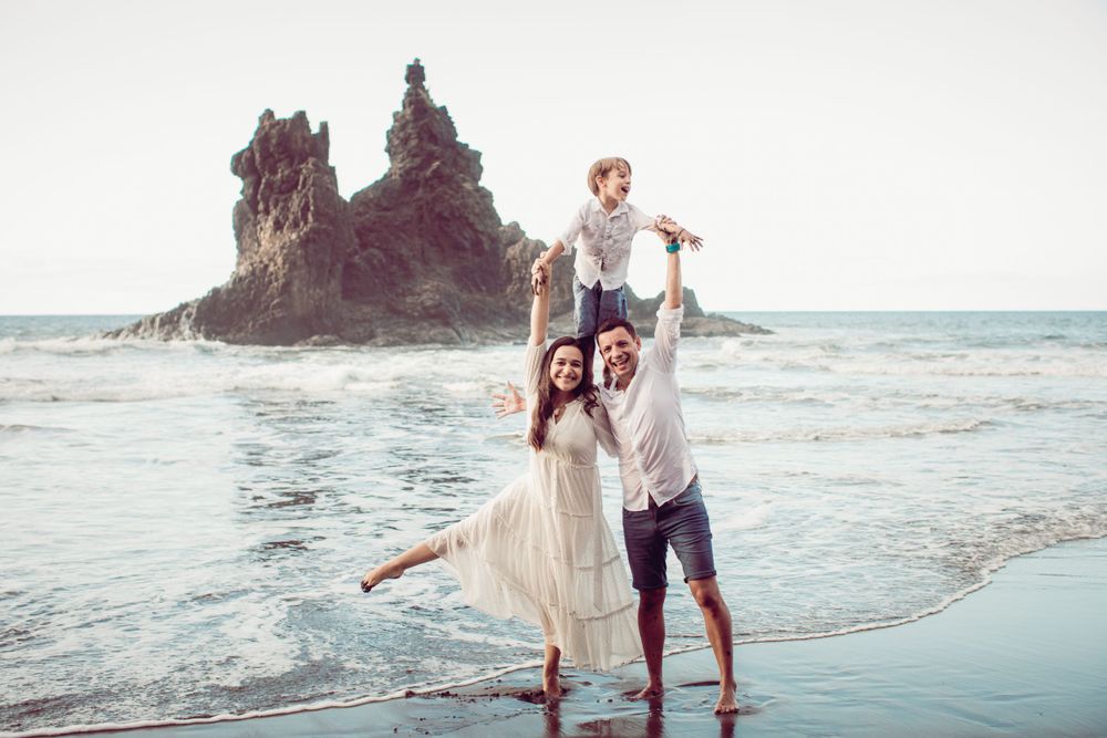 Playful family moment captured on a rocky beach at sunset with crashing waves.