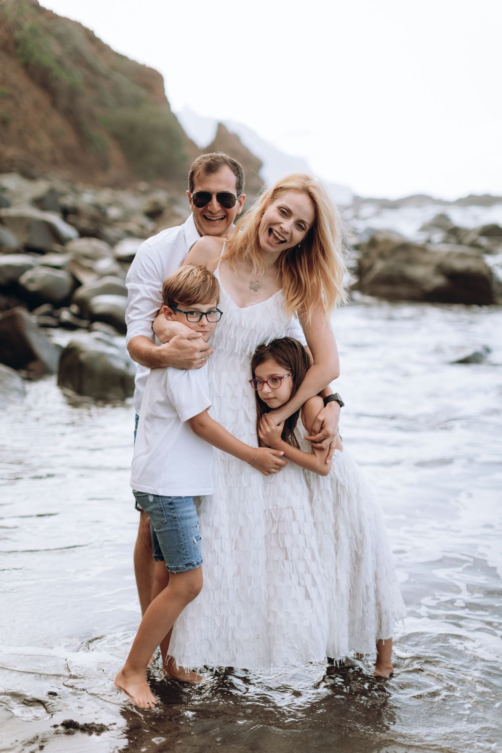 Family splashing and laughing together in white outfits at the beach.