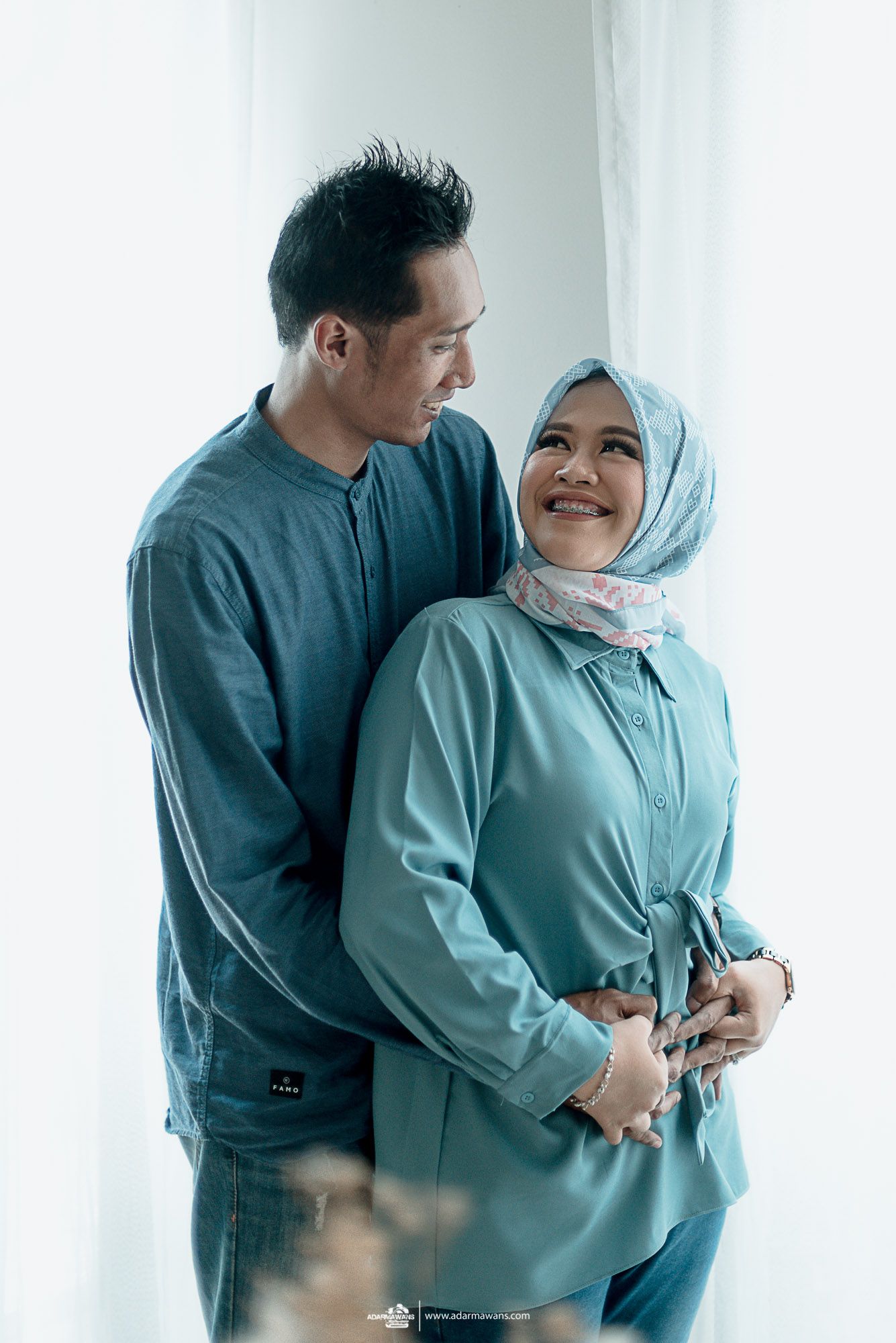 Intimate portrait of couple in matching blue outfits against white wall.