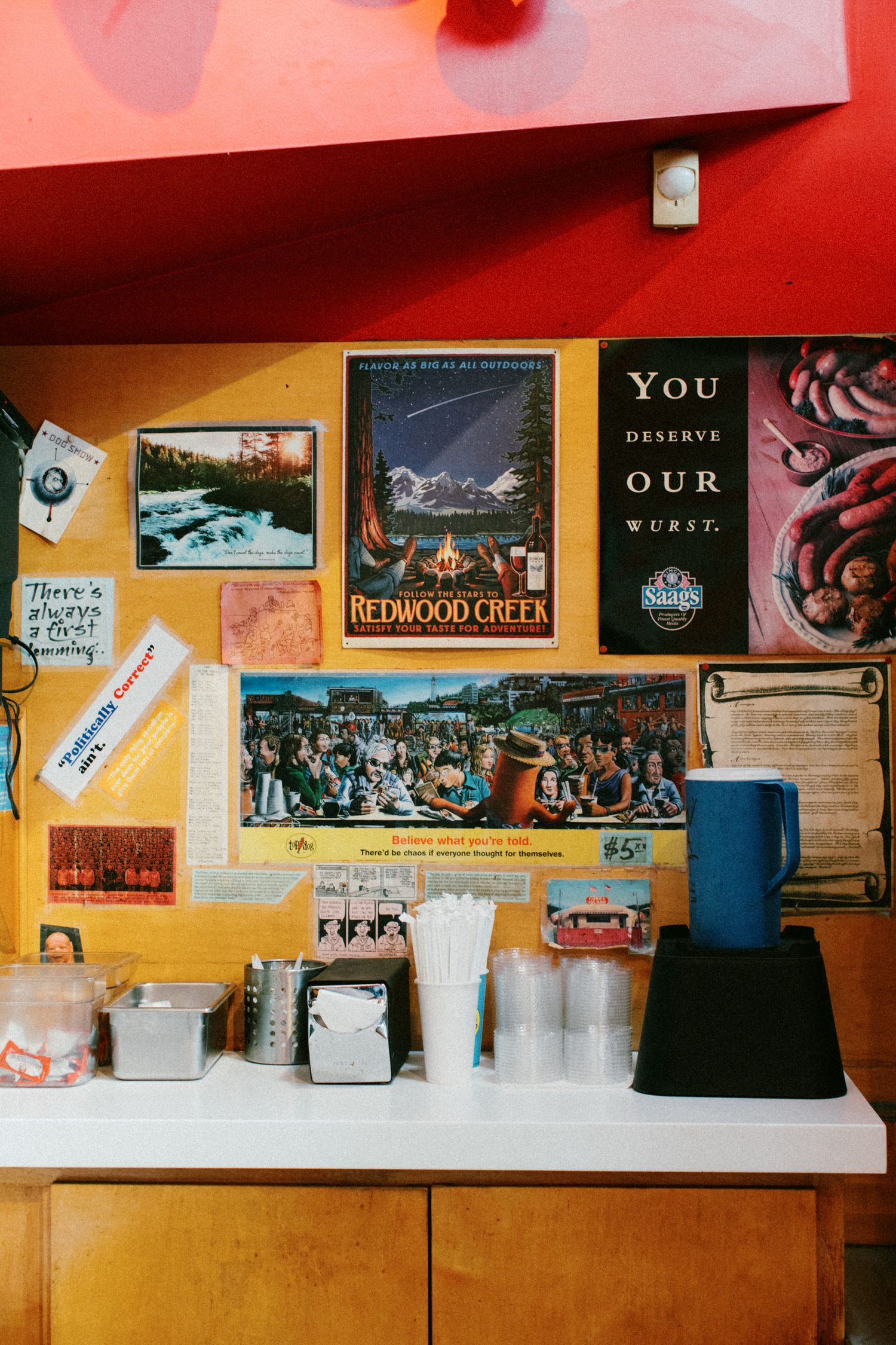 A yellow wall decorated with various posters, photos and artwork above a counter.