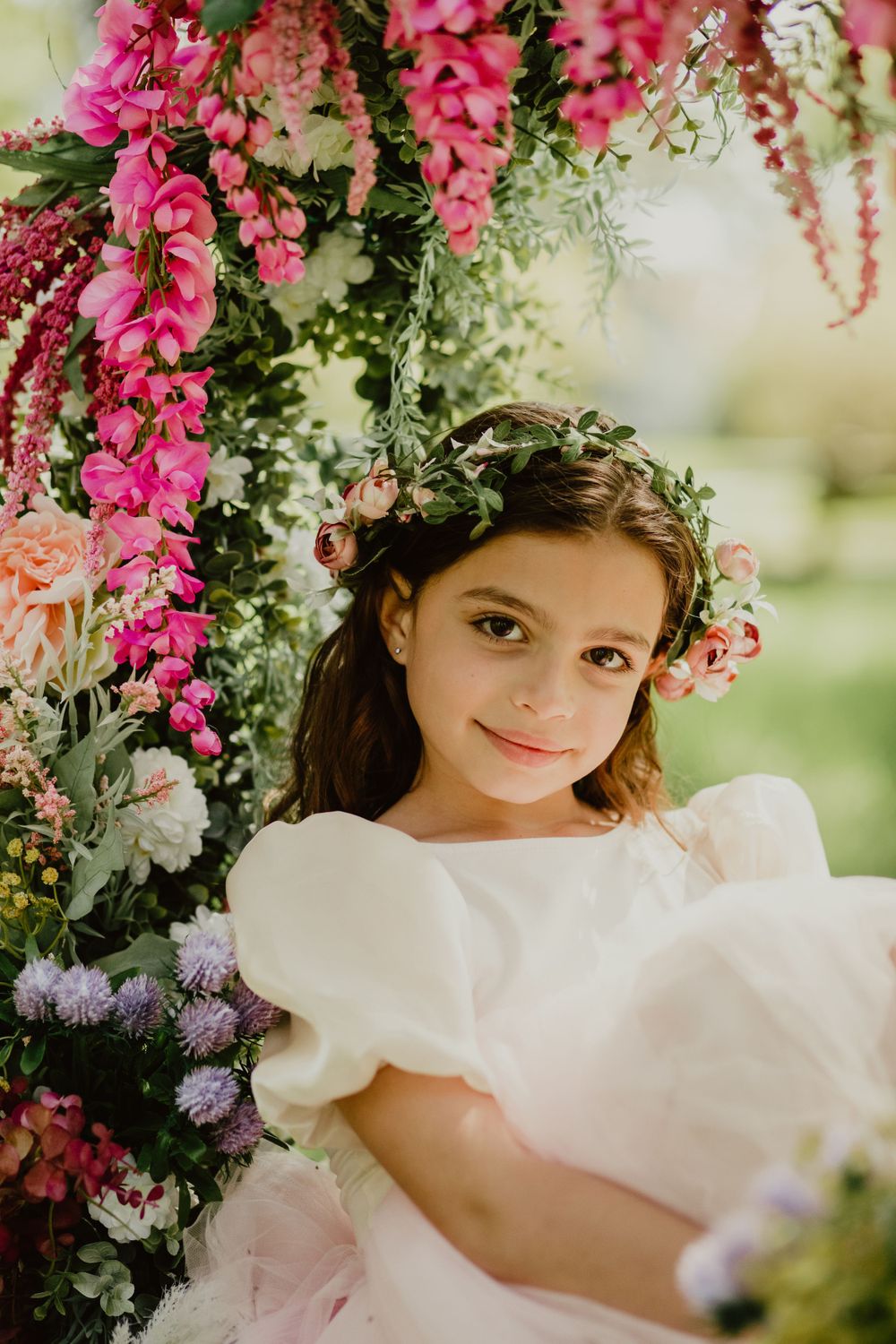 Person in white dress poses among cascading pink flowers in garden setting.