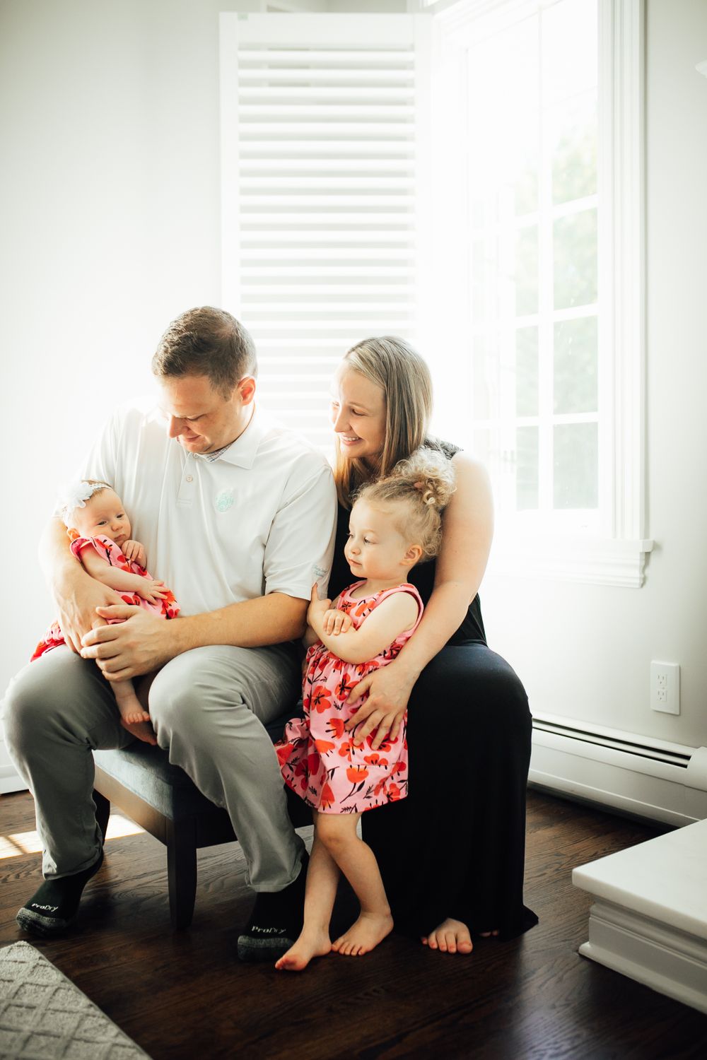 Family sitting together near a bright window, wearing coordinated outfits in a cozy living room setting.