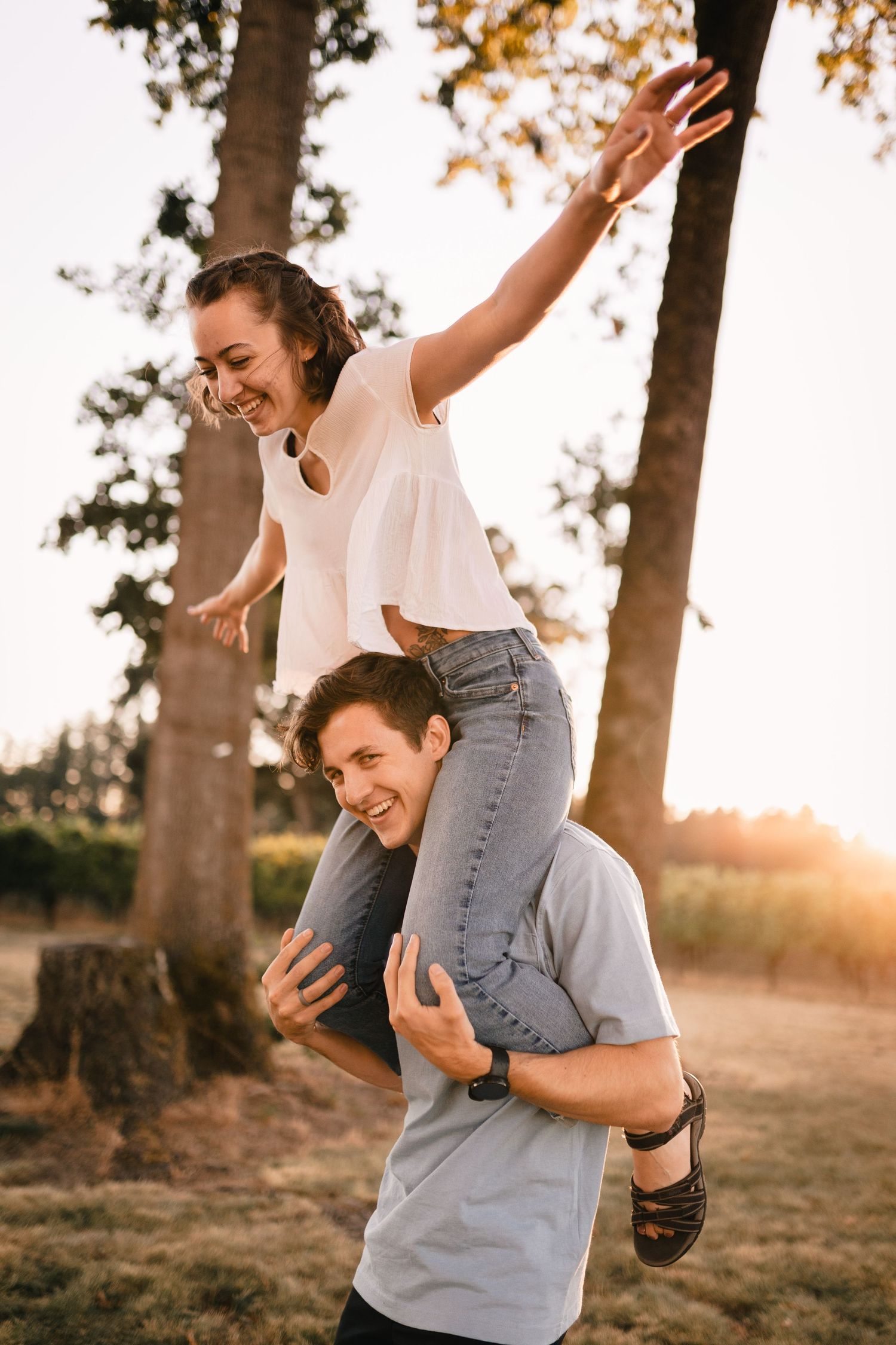 A playful moment captured as a couple enjoys a piggyback ride at sunset among trees.