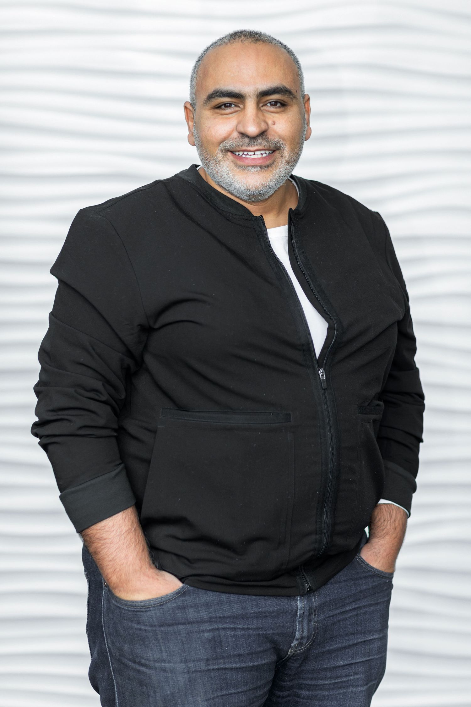 Professional headshot of person in black zip-up hoodie against white textured background.