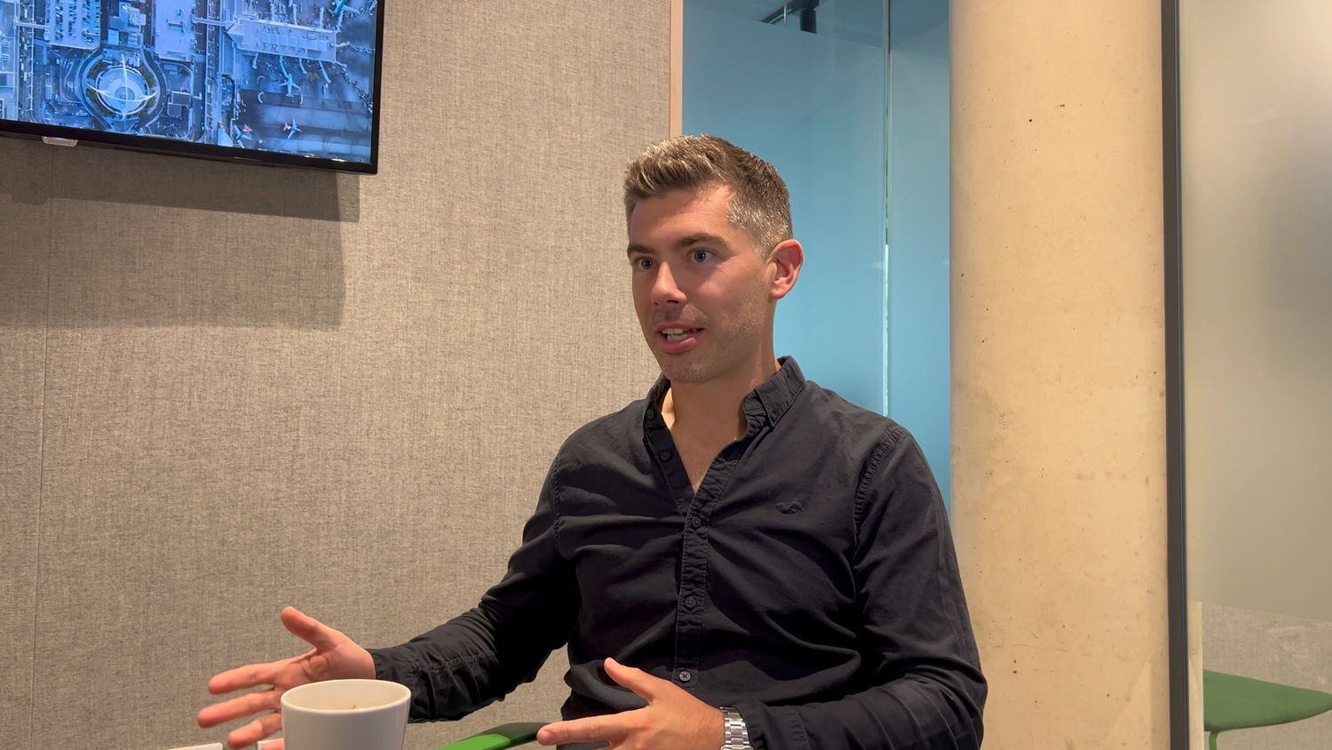 white man in room talking and moving his hands wearing a blue shirt