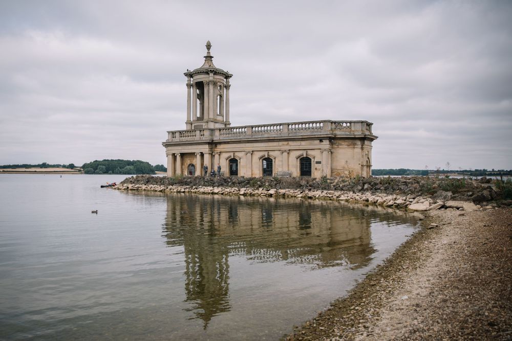 Historic stone church building with reflection in water on cloudy day at Normanton.