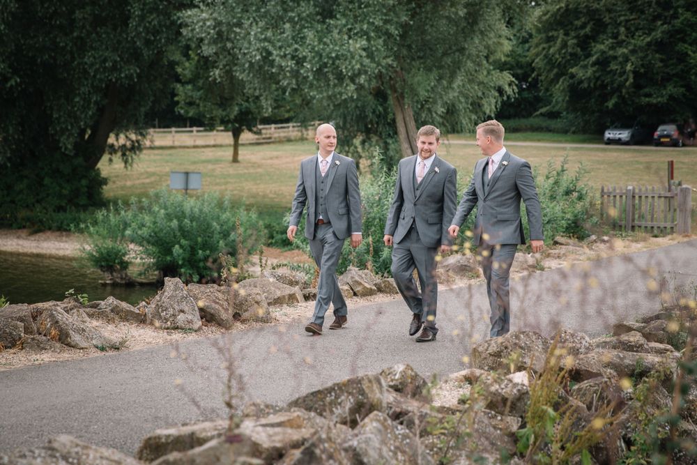 Three groomsmen walking along garden path wearing matching grey suits.