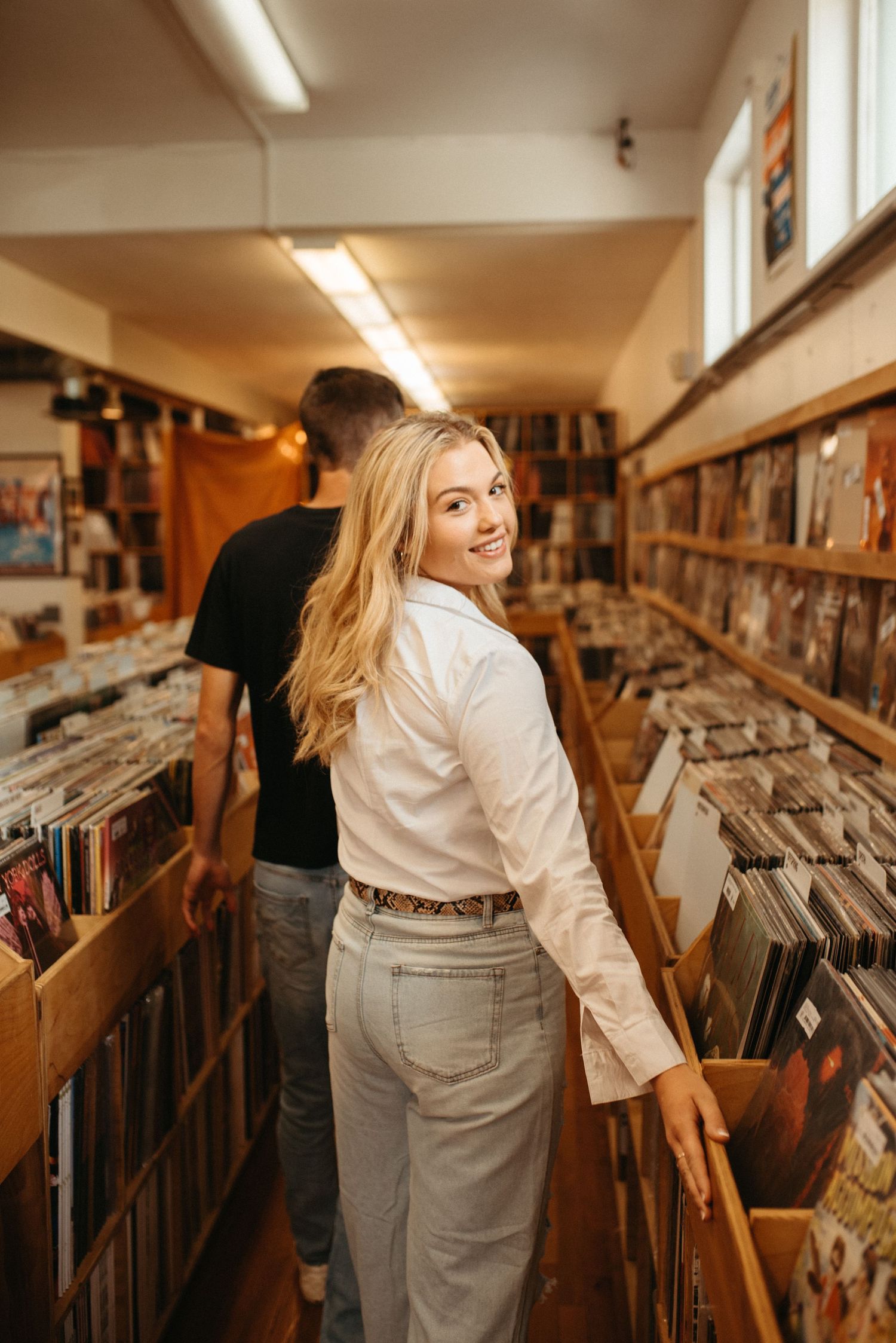 Two people browse vinyl records in narrow aisle of vintage record store with wooden shelving.