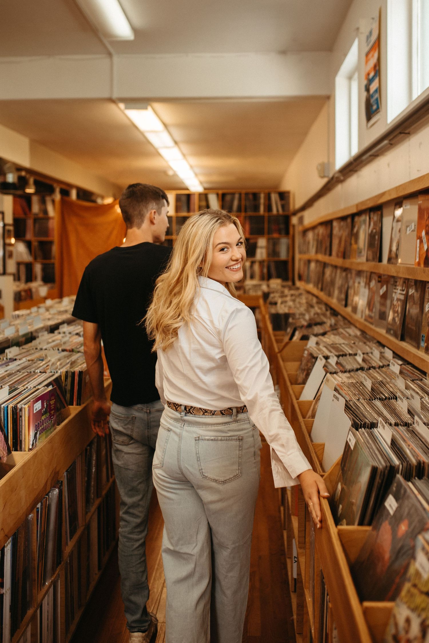 Customers explore vinyl collection in narrow aisle of record store with fluorescent lighting.