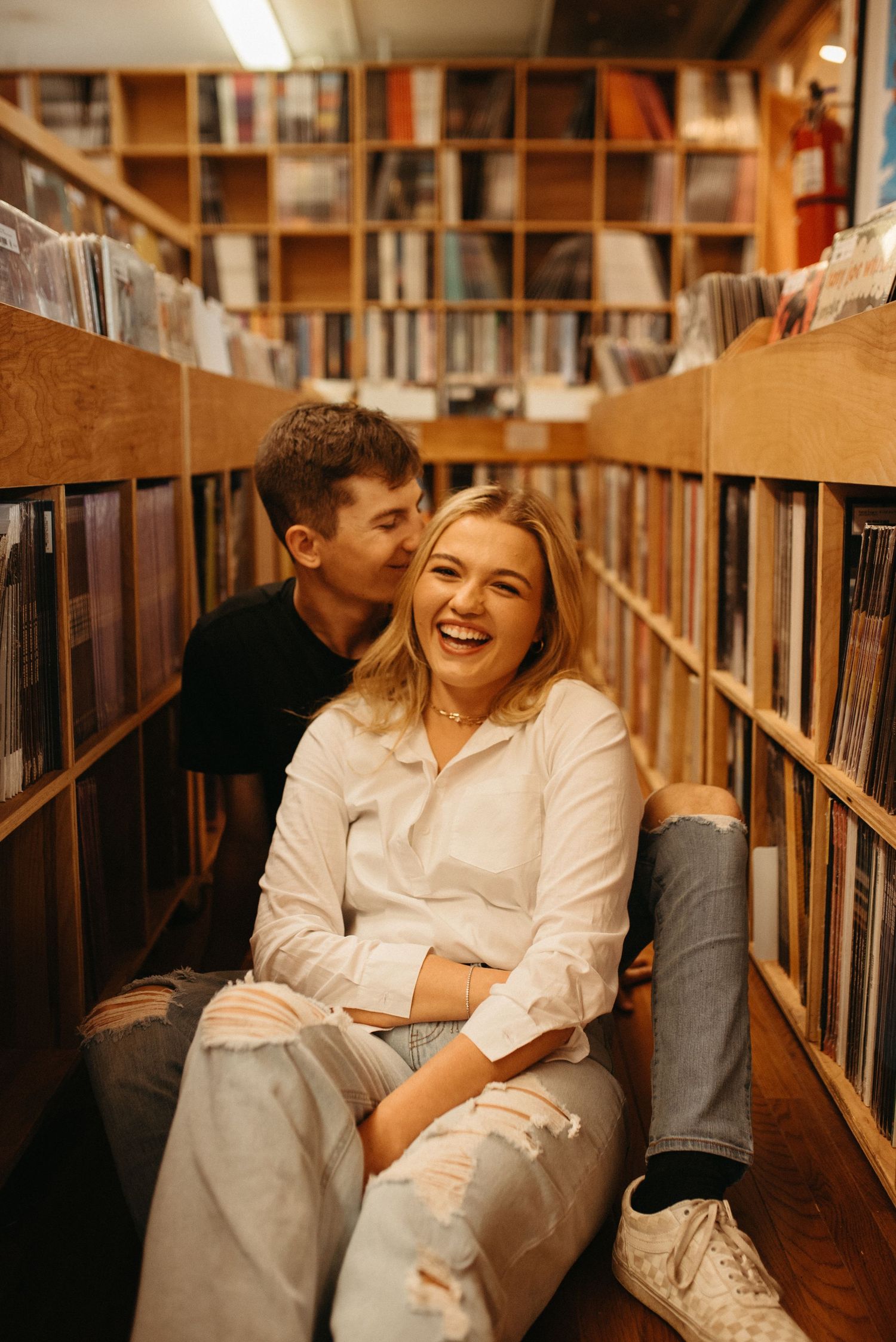 Couple shares joyful moment sitting between vinyl record bins in local music shop.