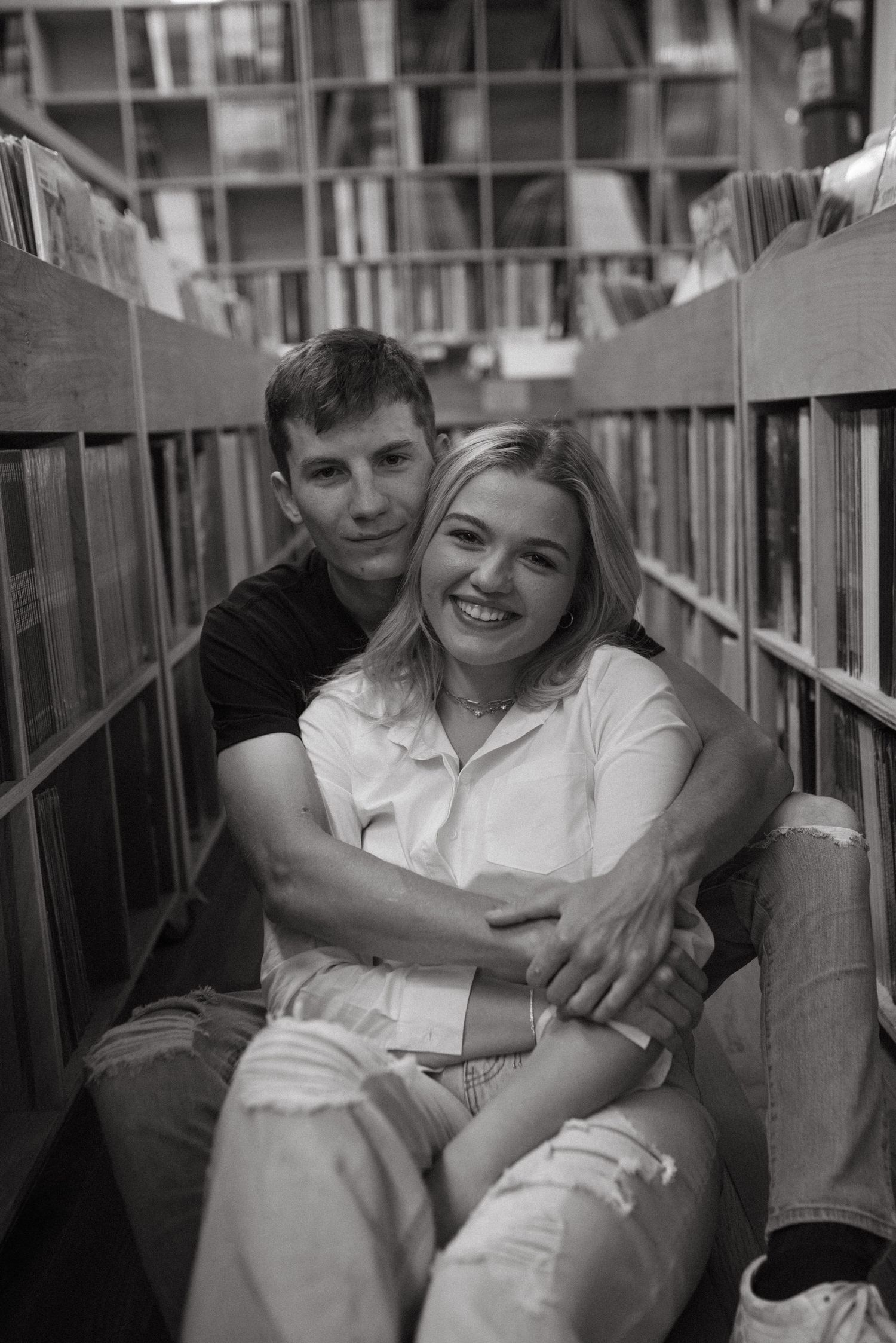 Two people share intimate moment while sitting between record bins in vintage music store.