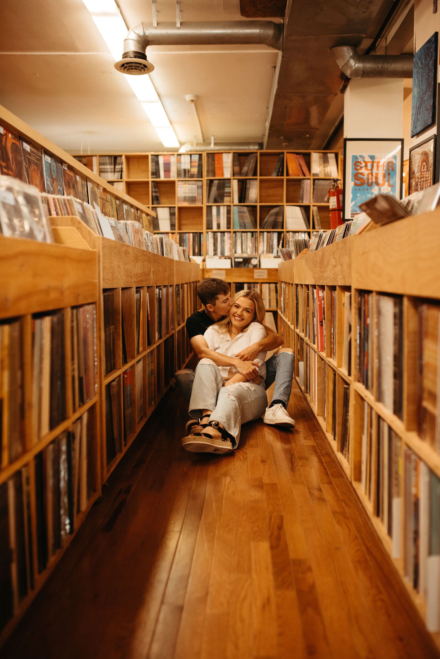 A romantic couple sitting on the floor between rows of vinyl records in a music store.