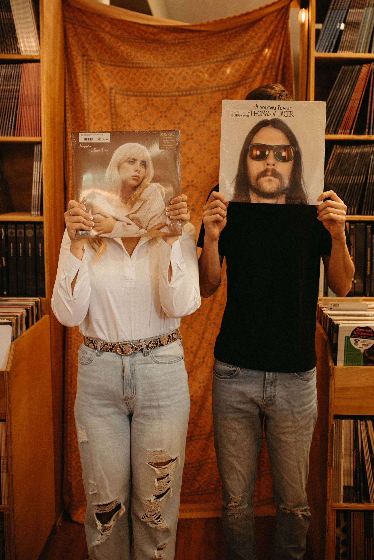 Two people holding vinyl album covers in front of their faces in a record store.