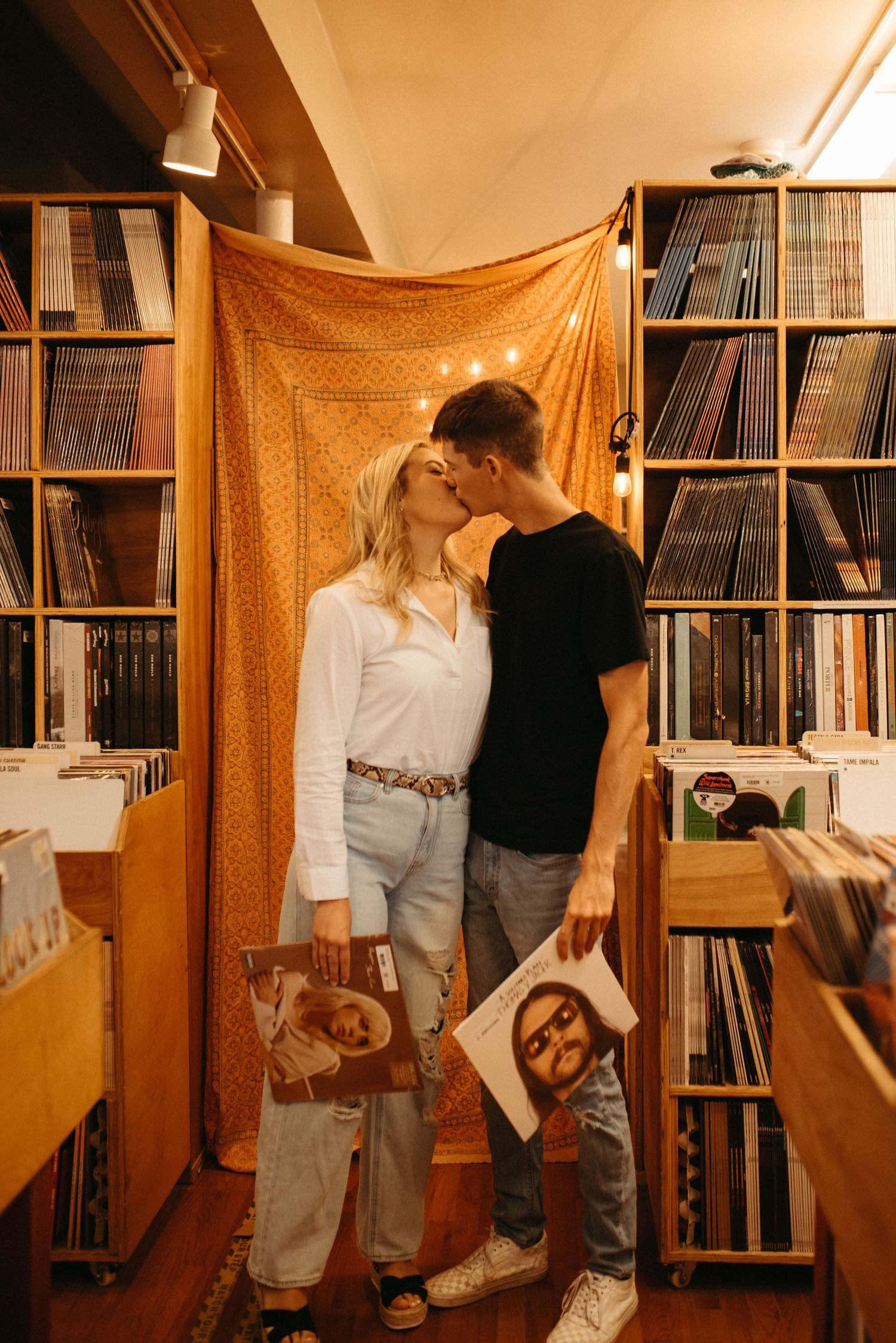 A couple sharing an intimate moment in a record store with vinyl-lined walls.