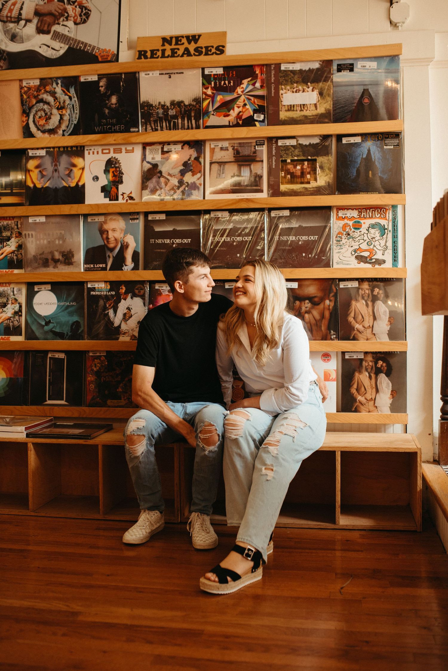 Two people sitting together on a bench surrounded by album covers in a record store.