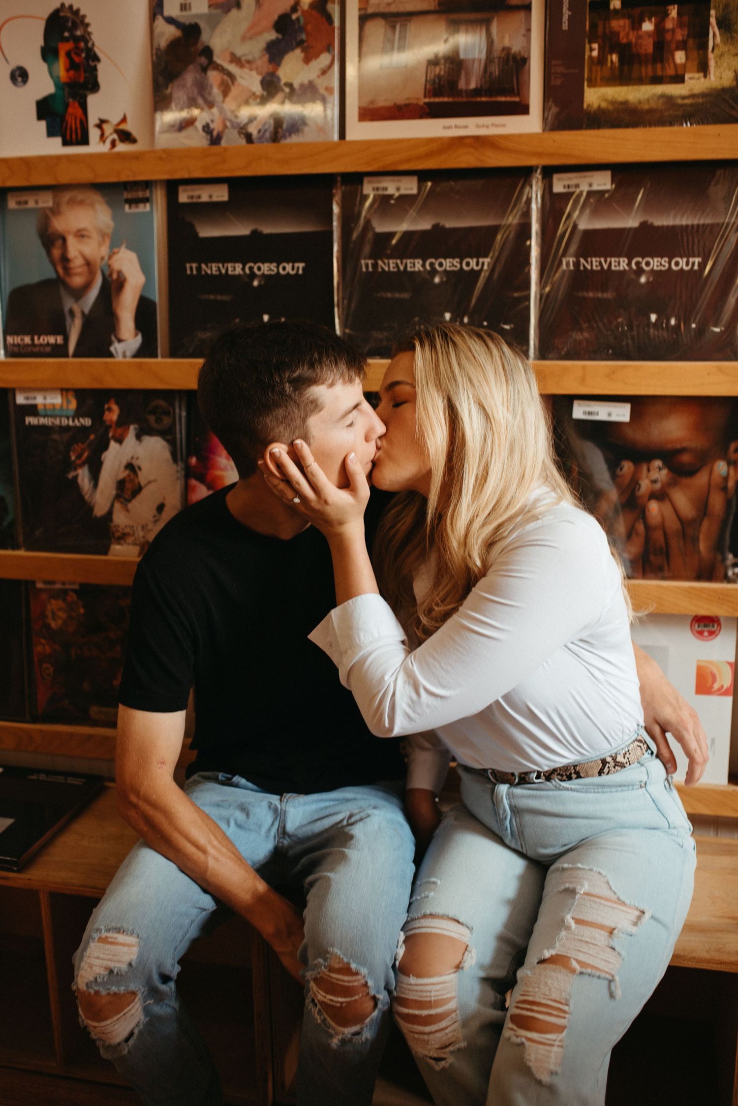 Romantic couple sharing an intimate moment in front of vintage album covers on display wall.