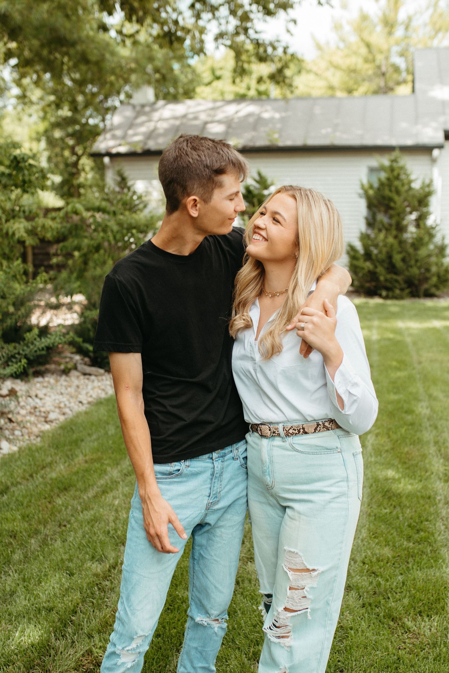 Playful couple in matching outfits laughing together in backyard garden setting.