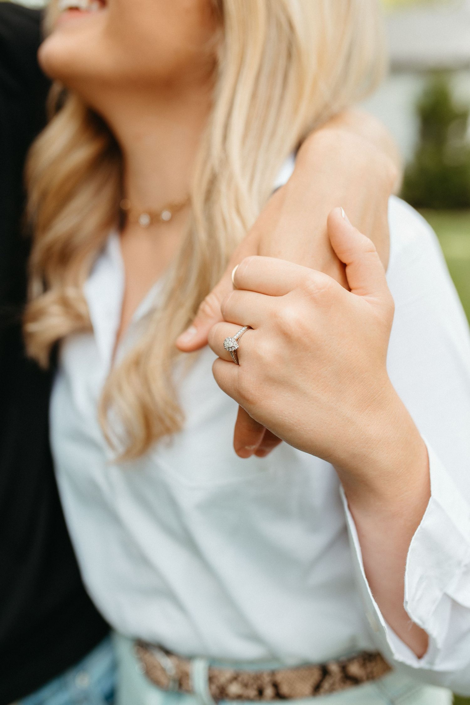 Close-up detail of hands and engagement ring with woman wearing white blouse and snakeskin belt.