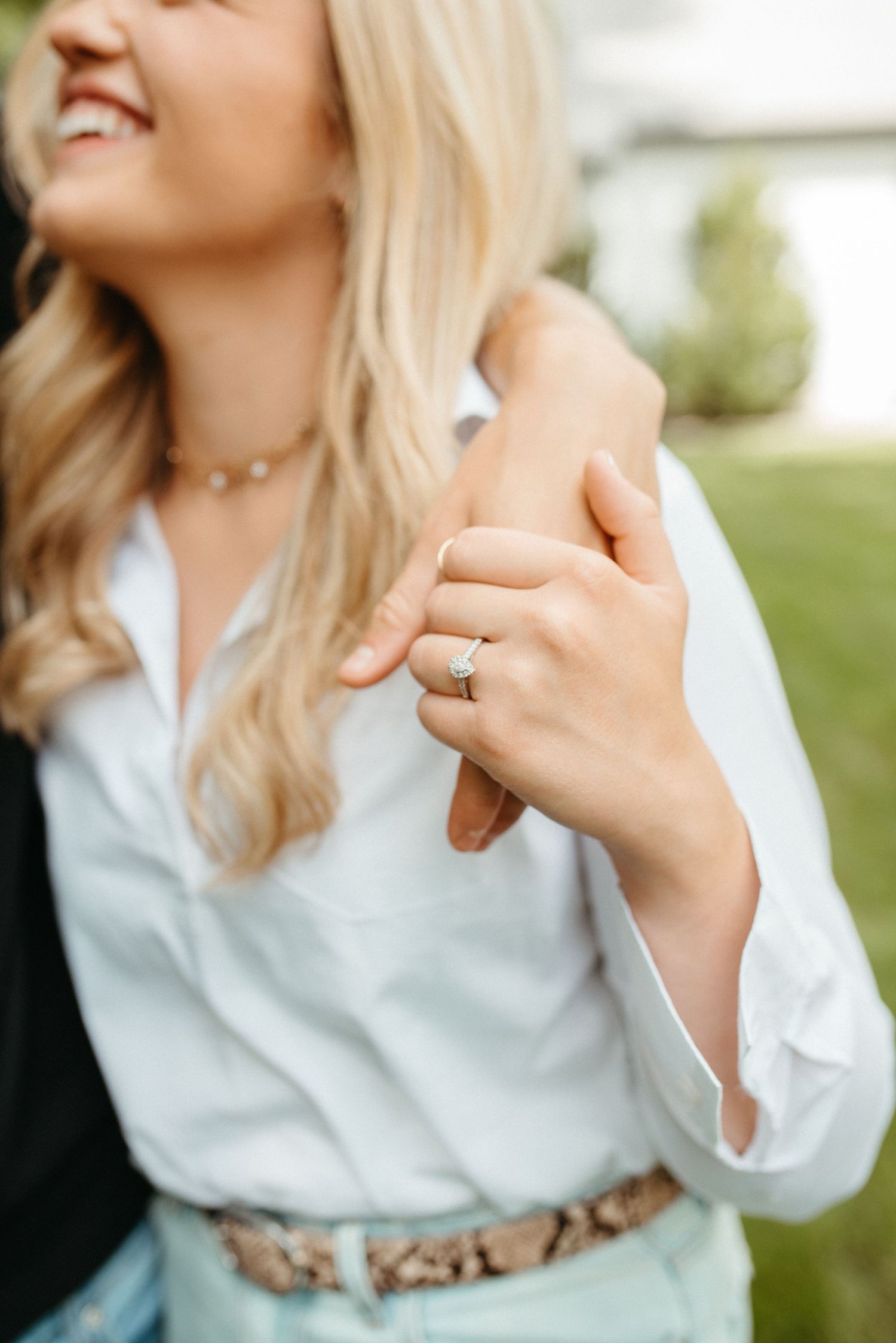 Detail shot of engagement ring and delicate necklace with white blouse and animal print belt.