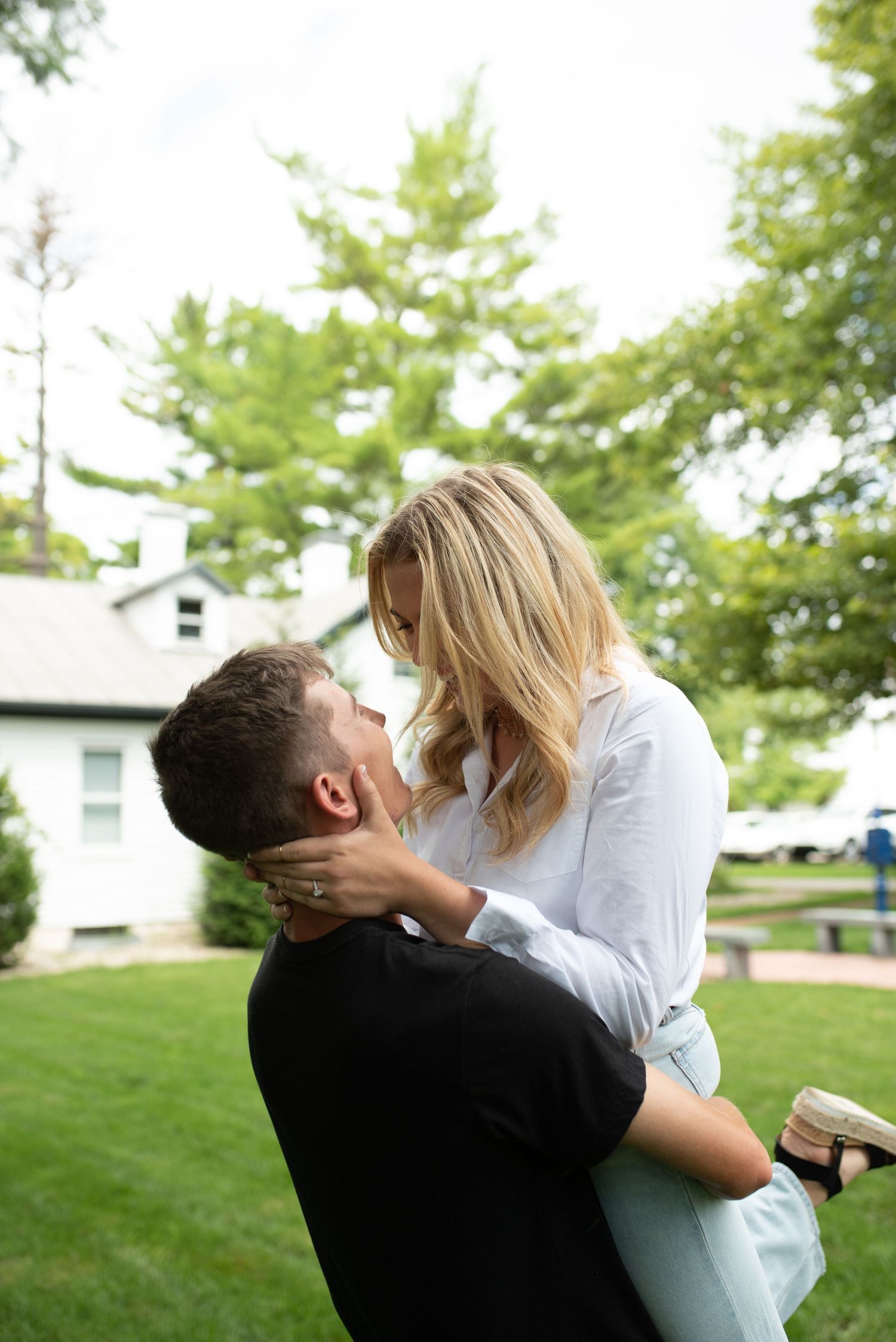 Couple sharing romantic embrace in sunny garden with white house in background.