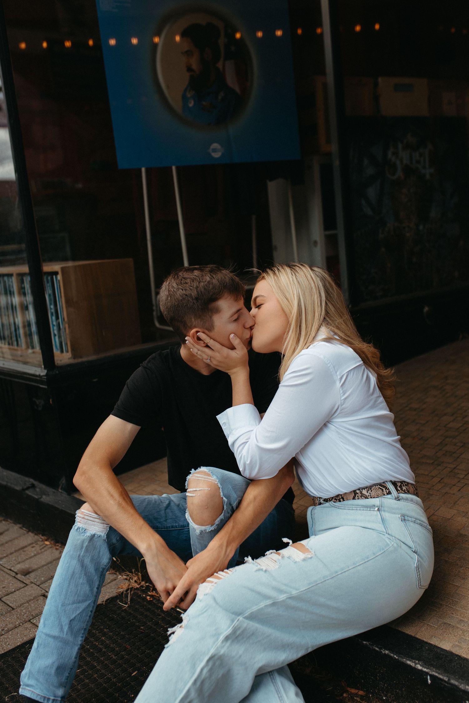 A tender moment captured outside a storefront with string lights.