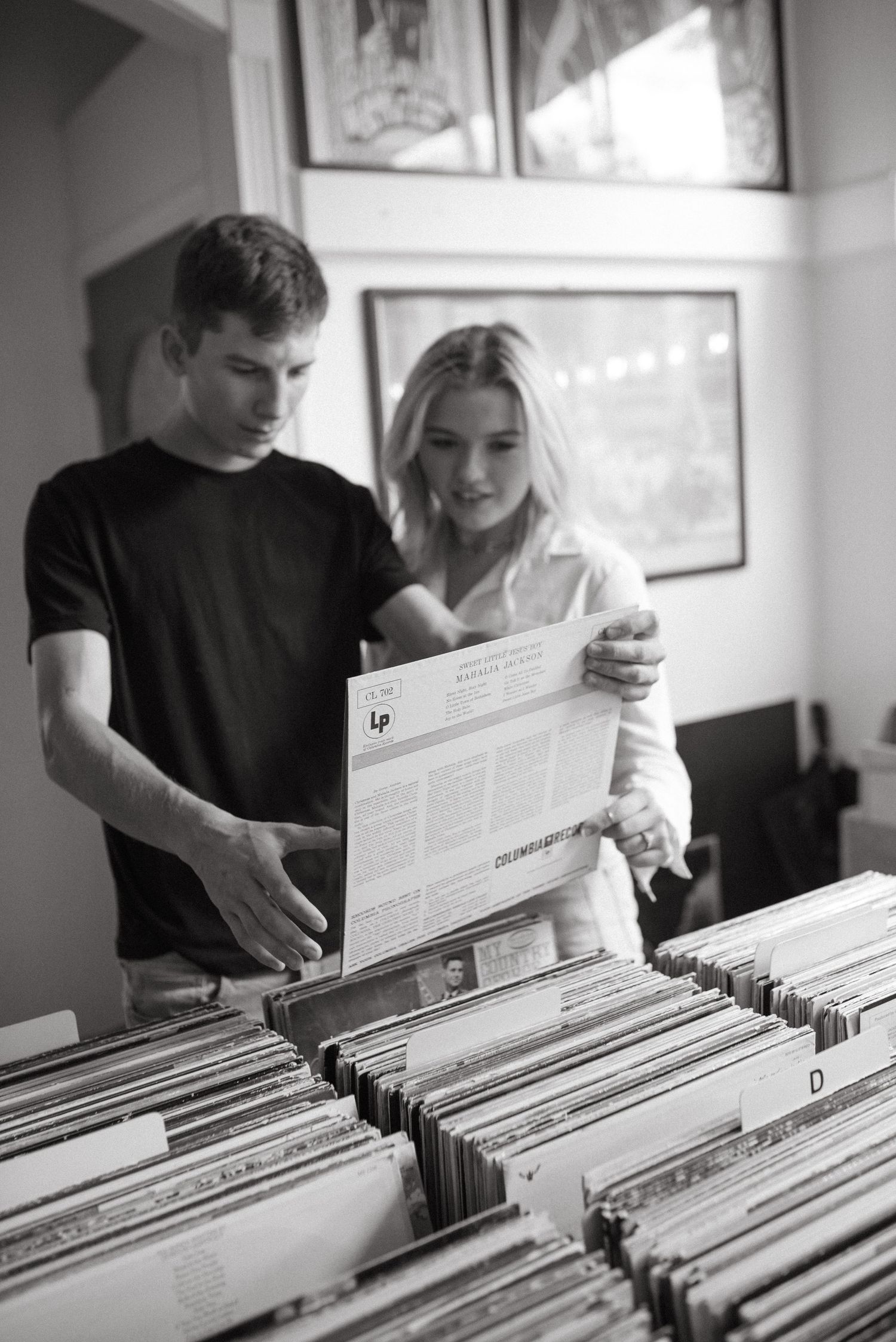 Two people examine album liner notes while browsing through vinyl records in black and white.