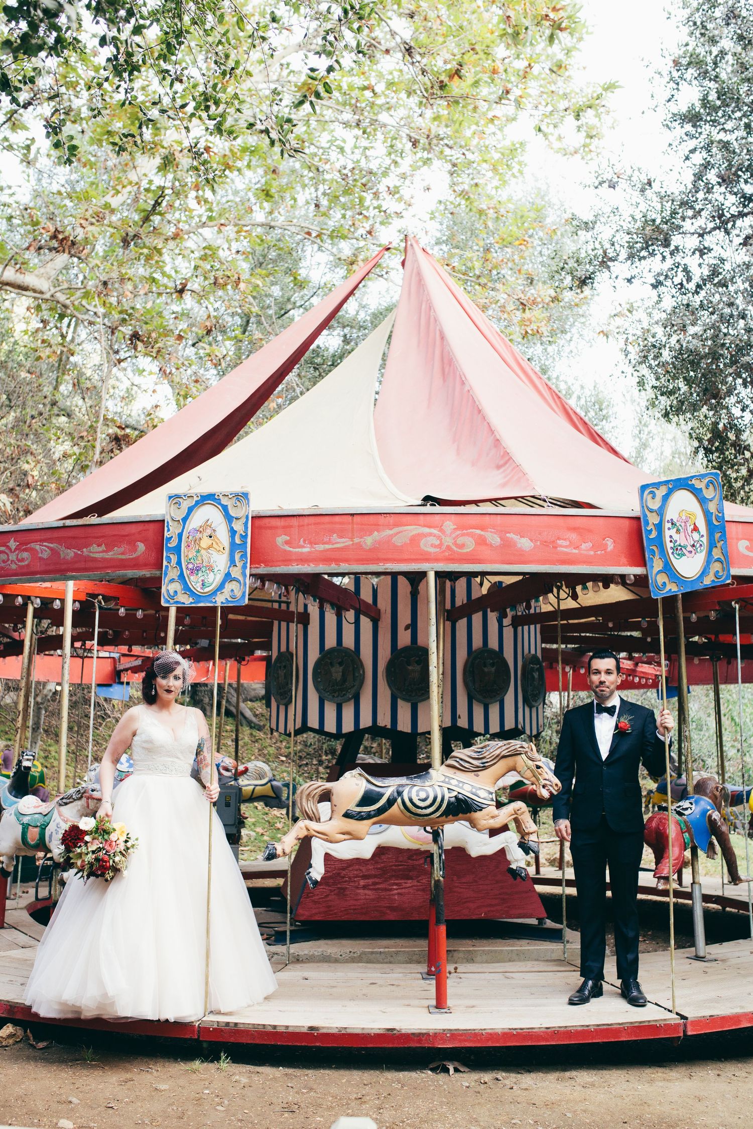 Wedding couple poses on vintage carousel with red and white striped tent top.
