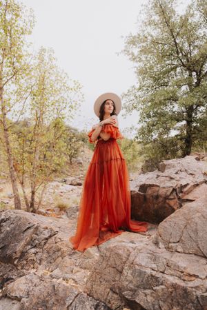 A dramatic orange gown stands out against natural rock formations and autumn trees.