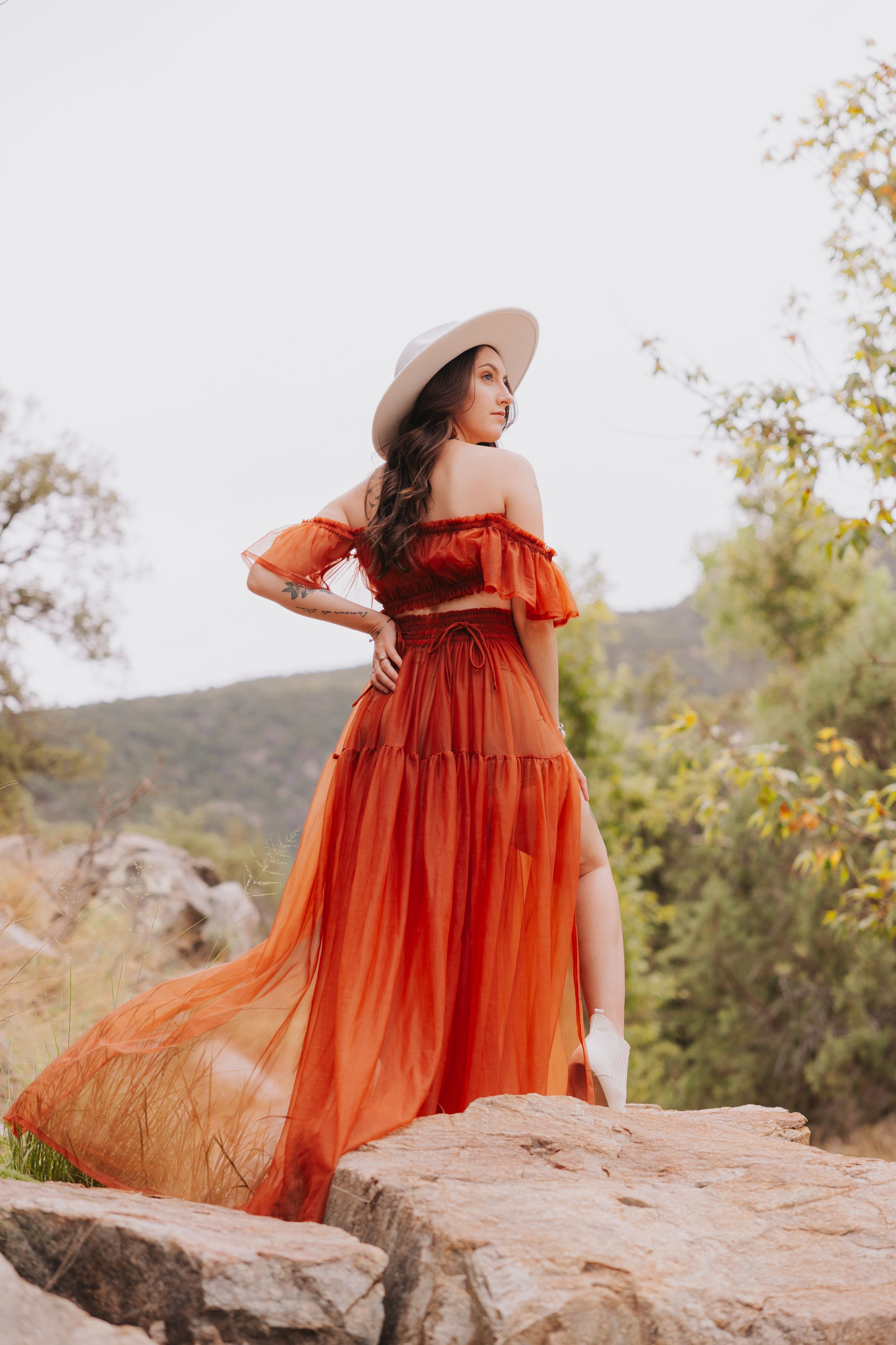A graceful pose on red rocks showcases a billowing rust-colored dress and wide-brimmed hat.
