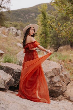 Flowing red dress creates movement against natural rock formations and mountain backdrop.