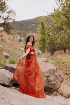 Ethereal red gown flows in the breeze against a mountainous natural landscape.