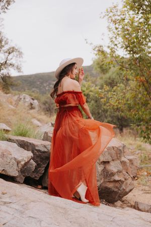 Graceful pose in flowing red dress against rustic mountain backdrop.
